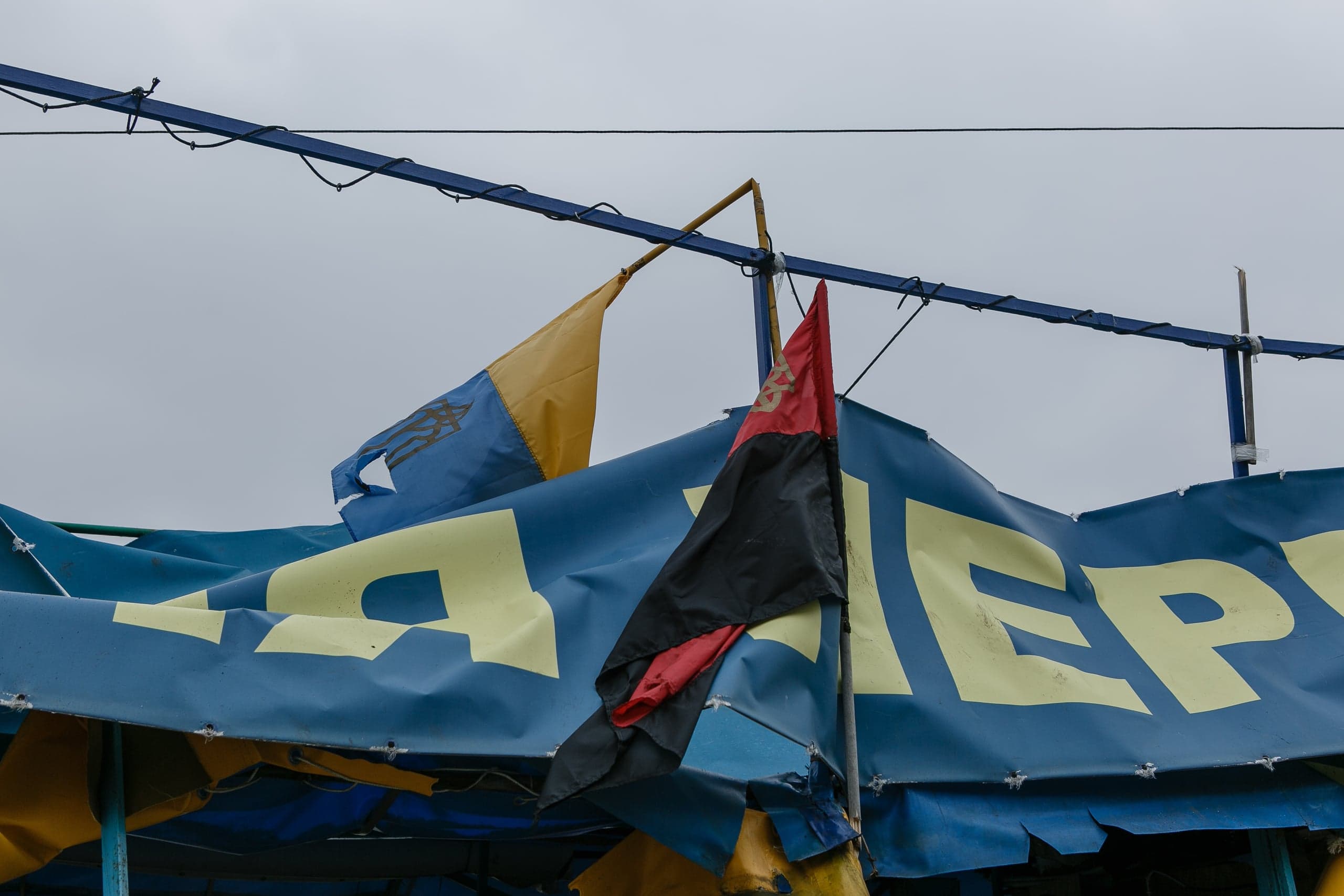 Потрепанный сине-желтый флаг с Тризубом и красно-черный флаг над синим тентом с желтыми буквами: "Я...ЕР".
