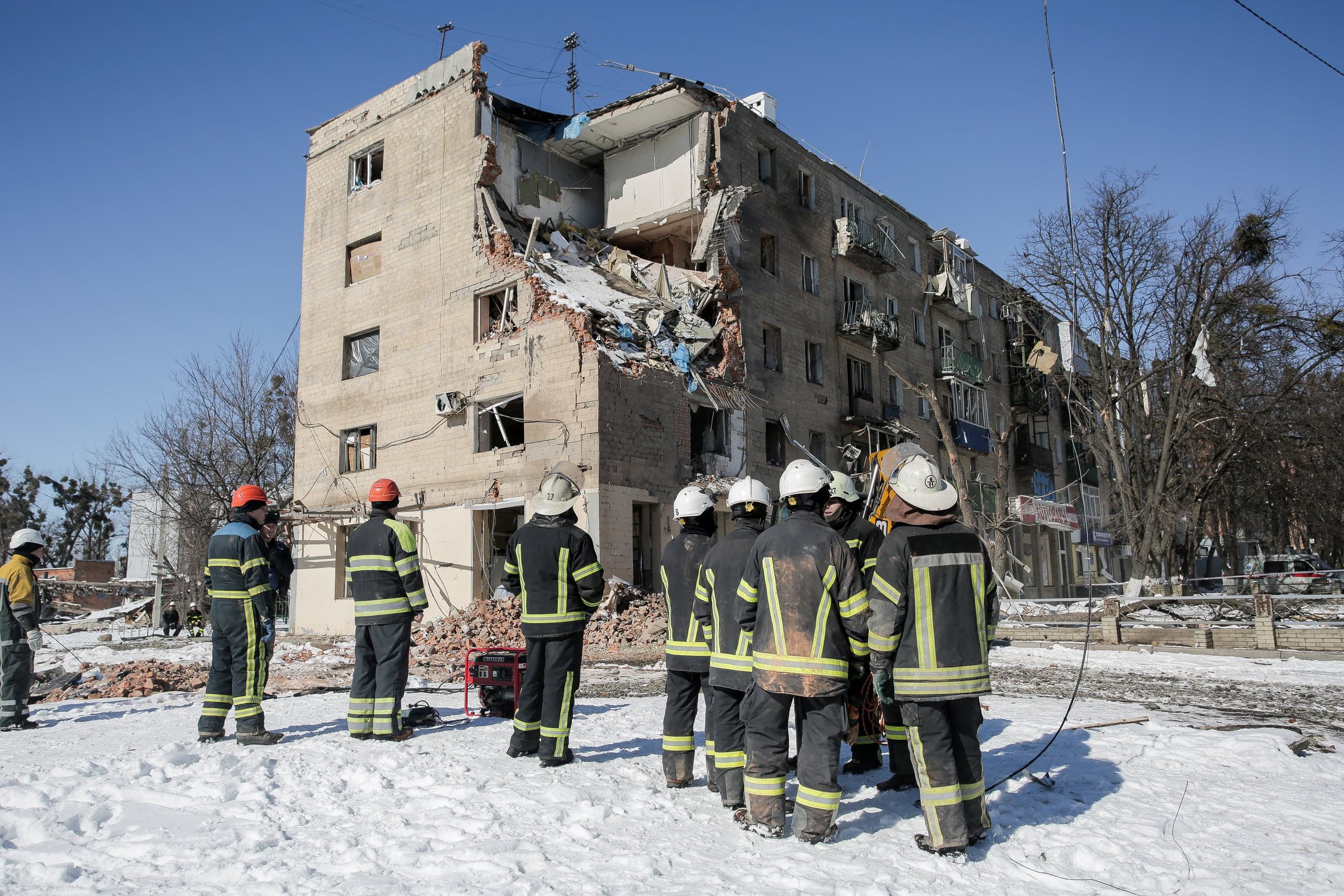 Группа спасателей стоит и смотрит на здание, большая часть угла которого разрушена