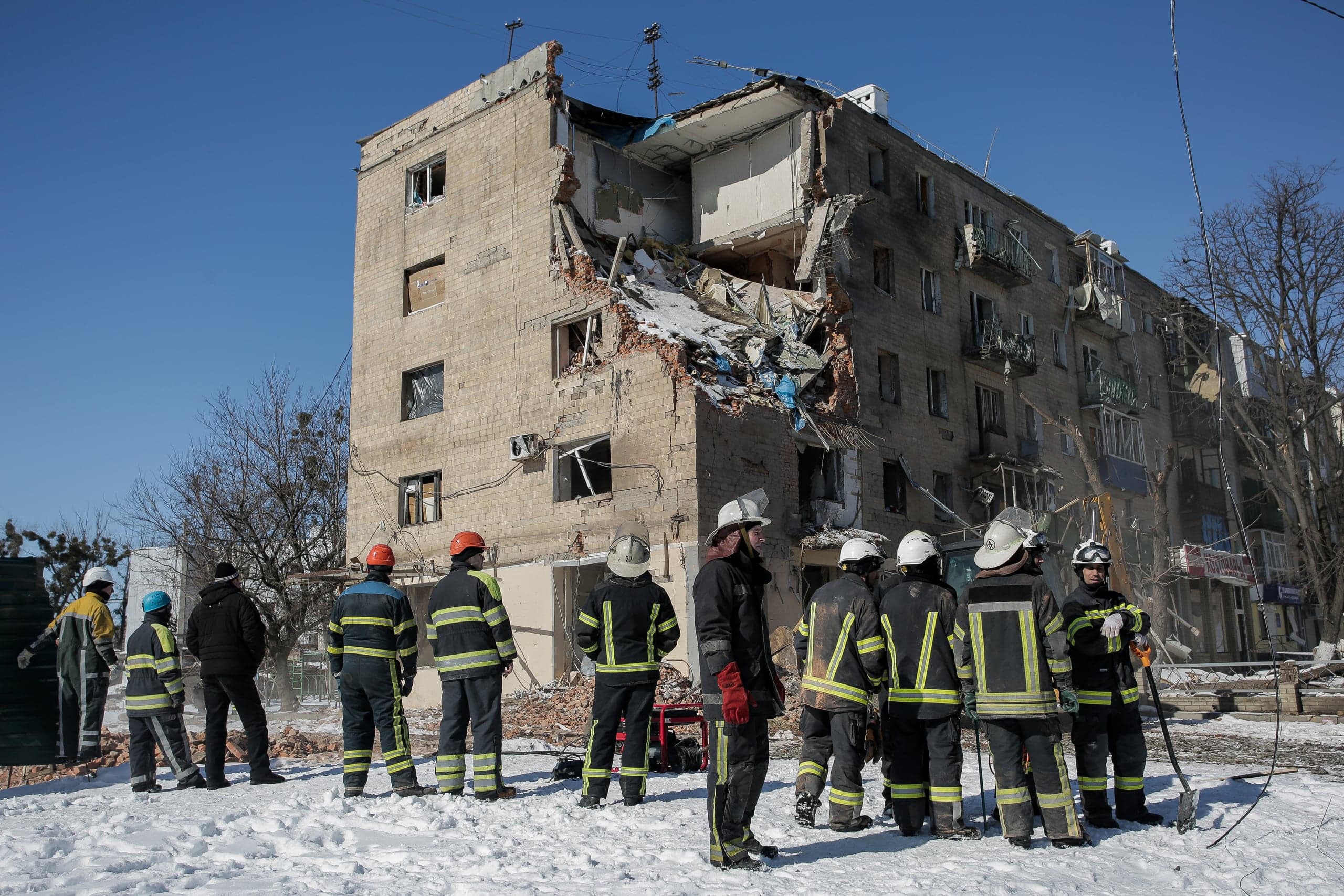 Спасатели на фоне частично разрушенного взрывом жилого дома в зимний день.
