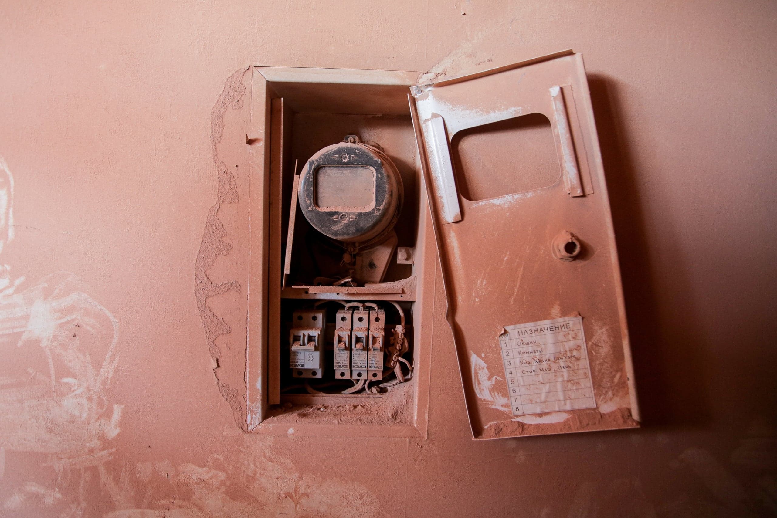 Оранжевая стена с открытой электрической коробкой, внутри счетчик и автоматы