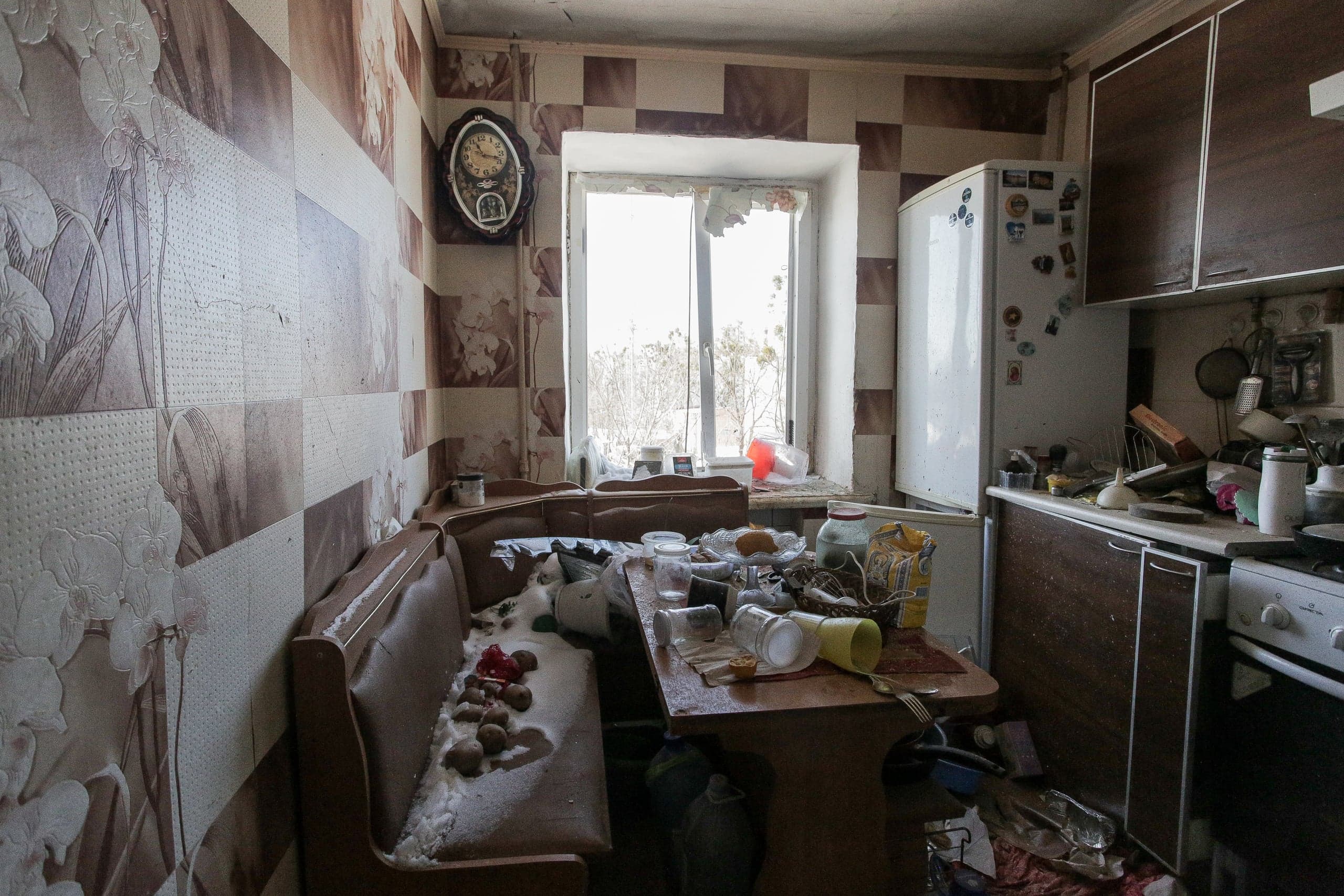 Разгромленная, заваленная мусором кухня с разбитым окном. На угловом диване и столе лежит снег и грязь.