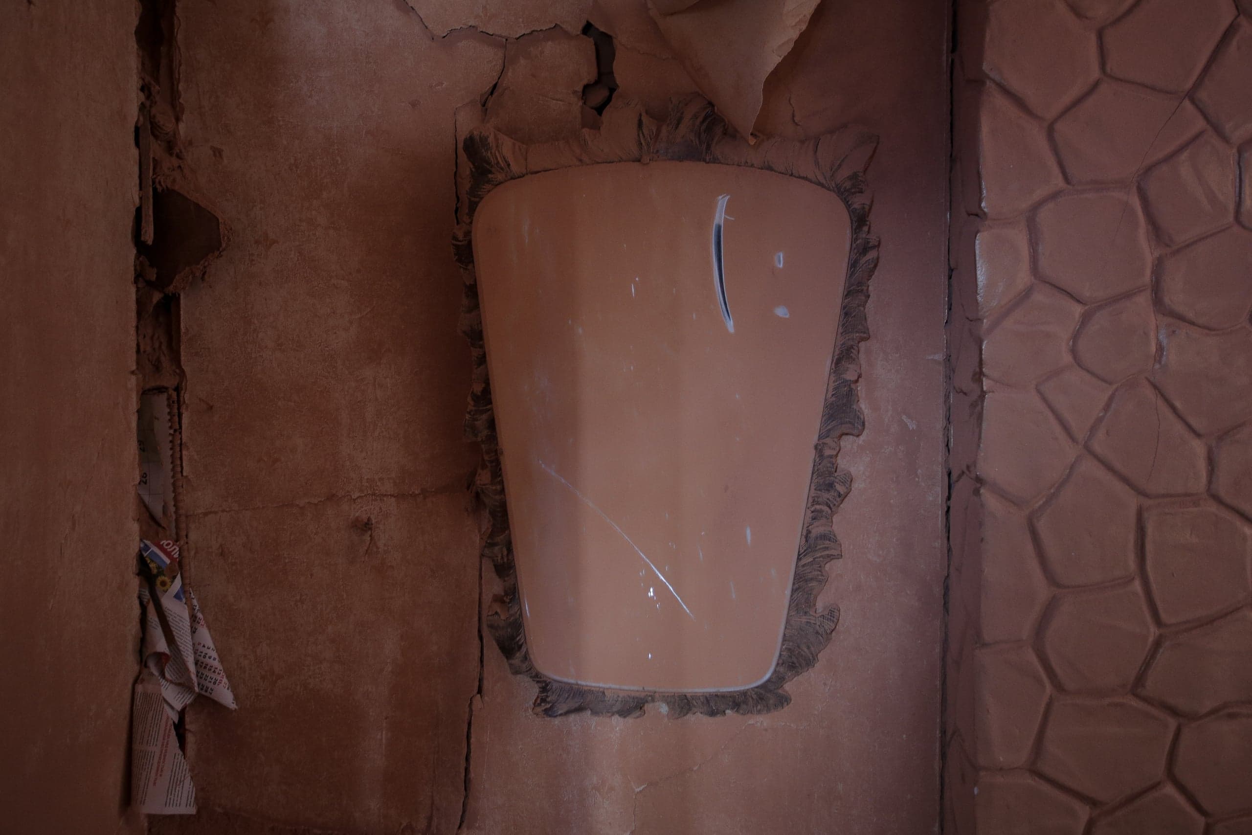 Вертикальная бежевая панель (возможно, остатки зеркала) на разрушающейся коричневой стене. Справа — стена с рельефным узором под камень.