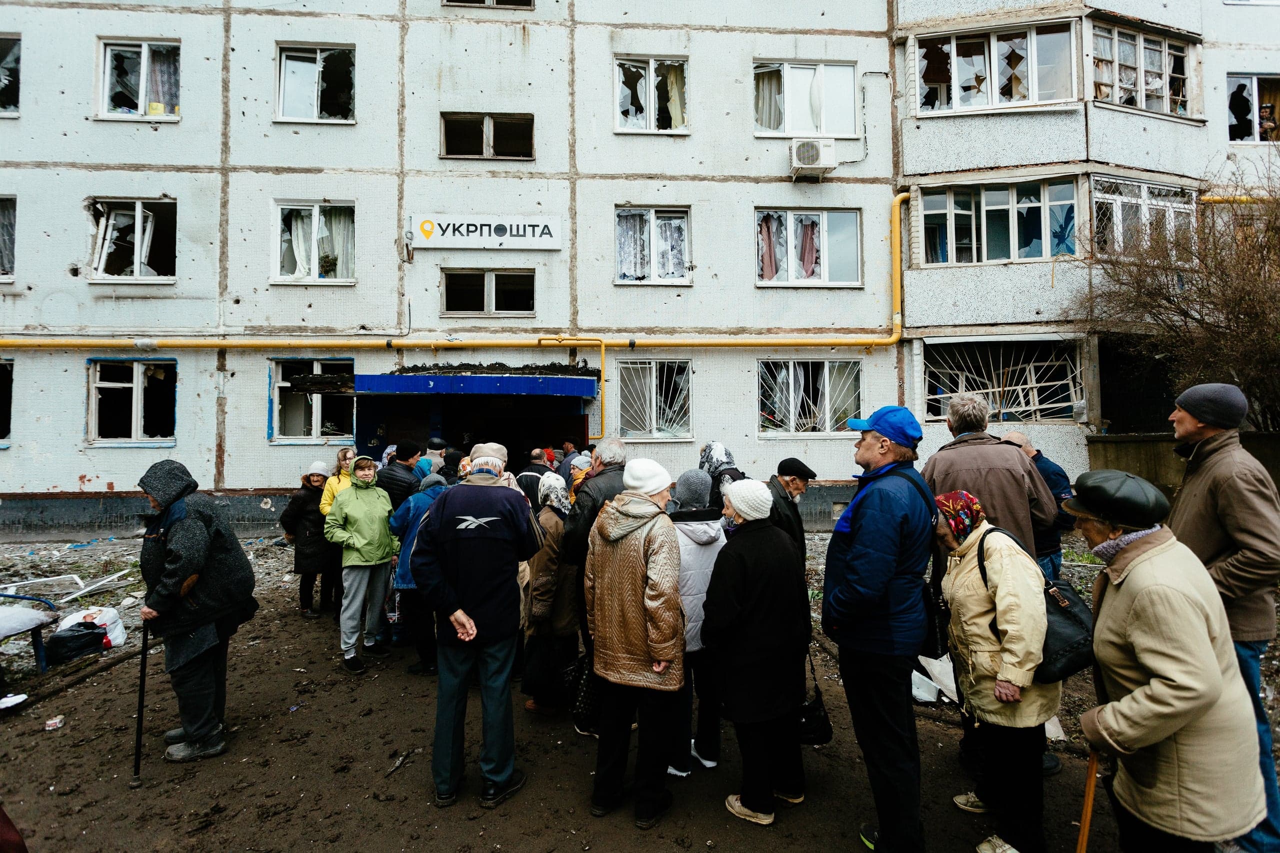 Очередь людей перед поврежденным обстрелами отделением "УКРПОШТА" с разбитыми окнами.