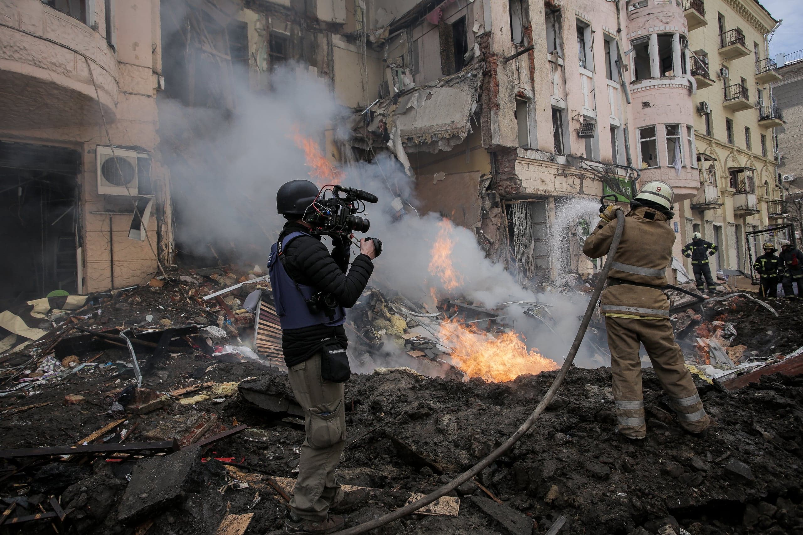 Оператор и пожарный на фоне разрушенного, горящего здания.