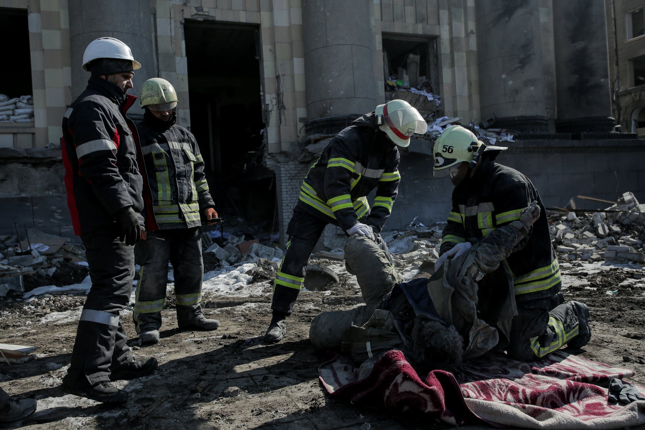 Спасатели оказывают помощь пострадавшему на земле среди обломков разрушенного здания.