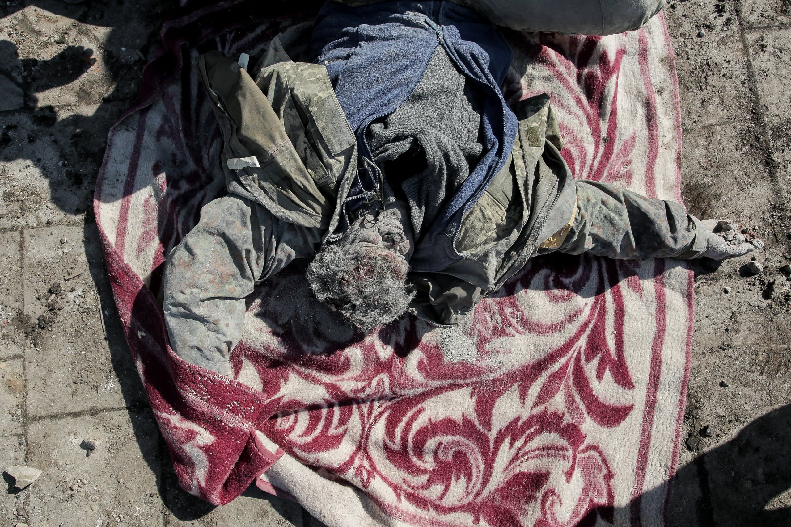 Запыленный труп человека лежит на красном покрывале на асфальте