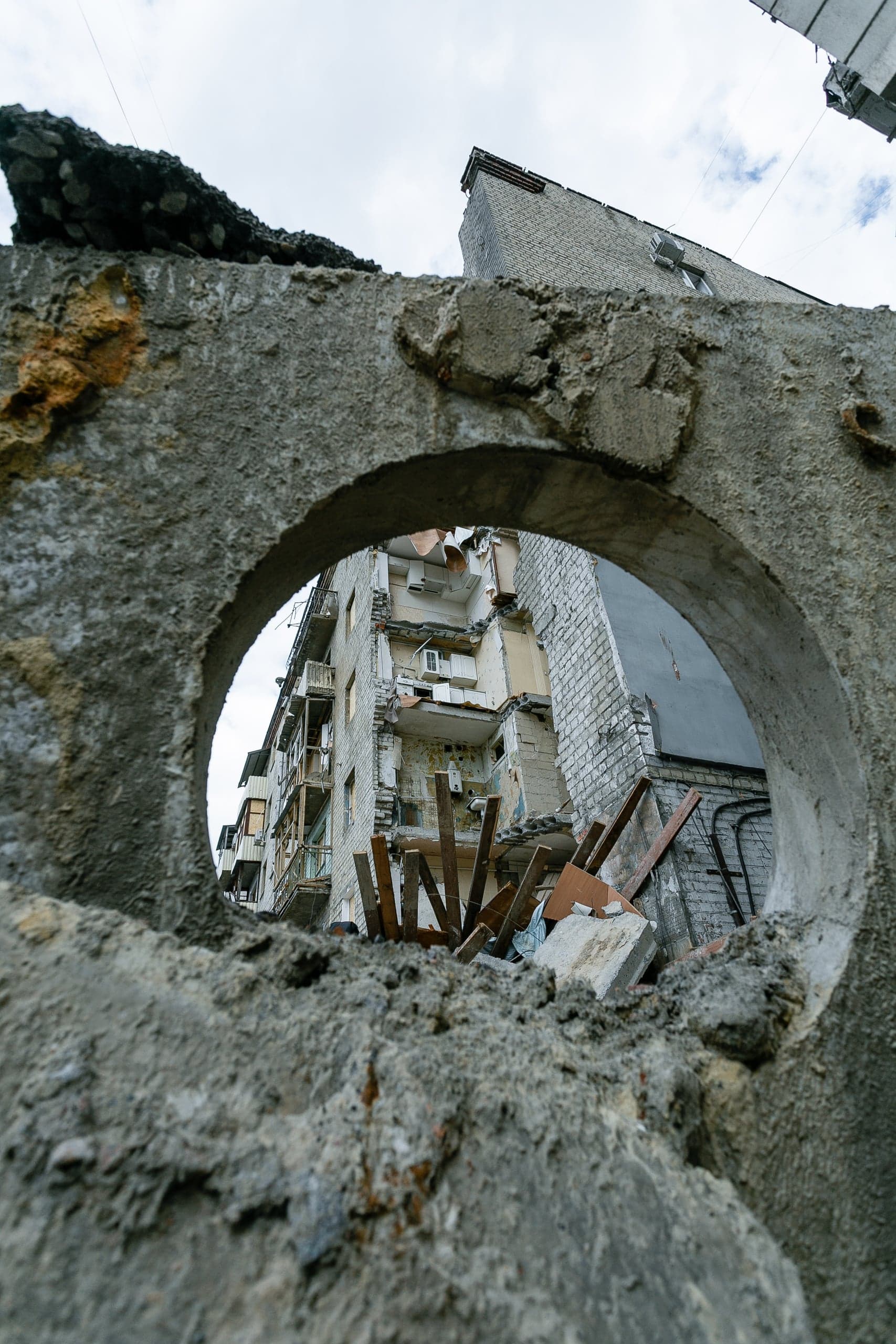 Сильно разрушенный жилой дом, видимый сквозь круглое отверстие в обломке бетона.