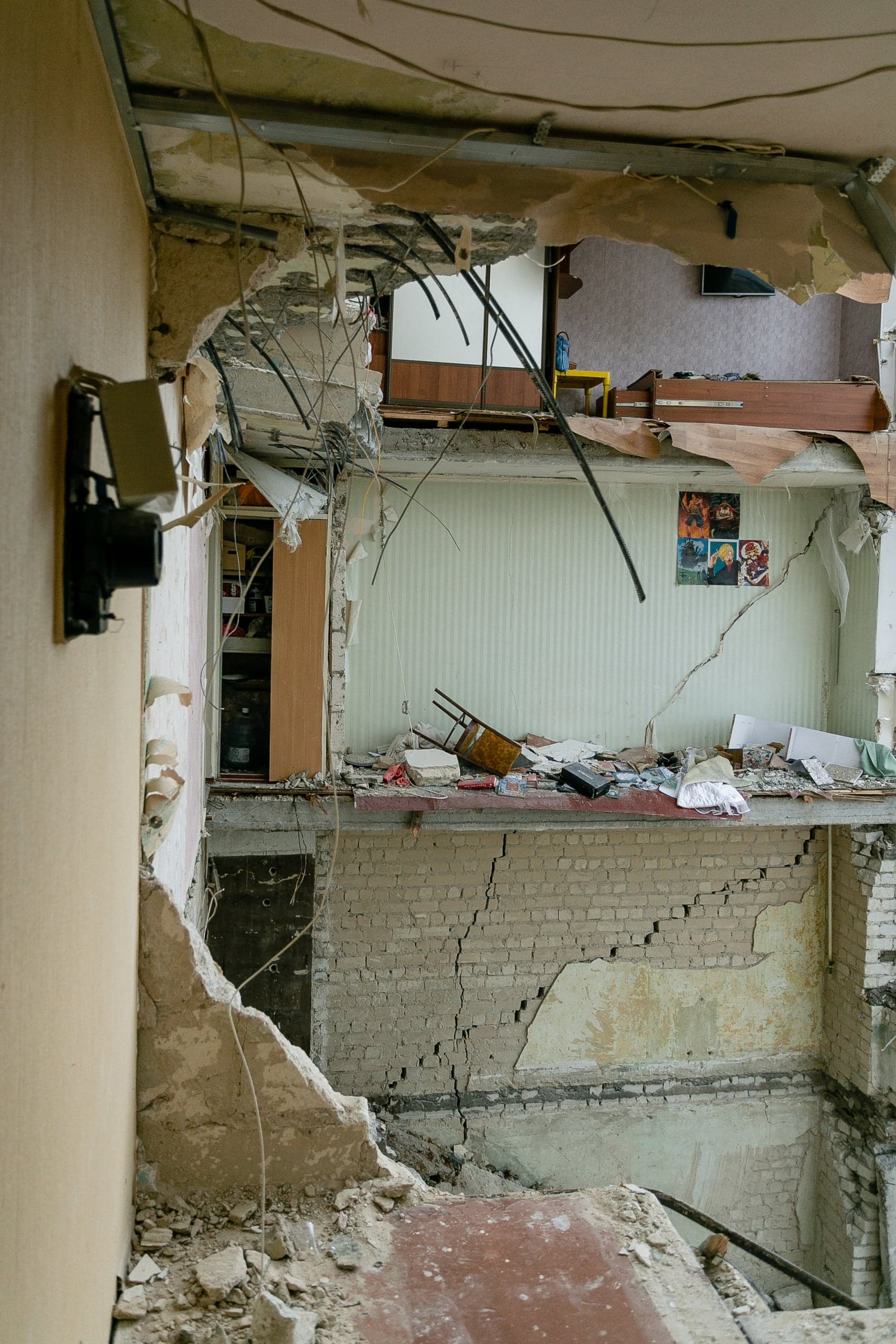 Разрушенные перекрытия и стены внутри многоэтажного жилого дома. Видны обломки, обнаженная арматура, висящие провода и глубокие трещины на кирпичной кладке.