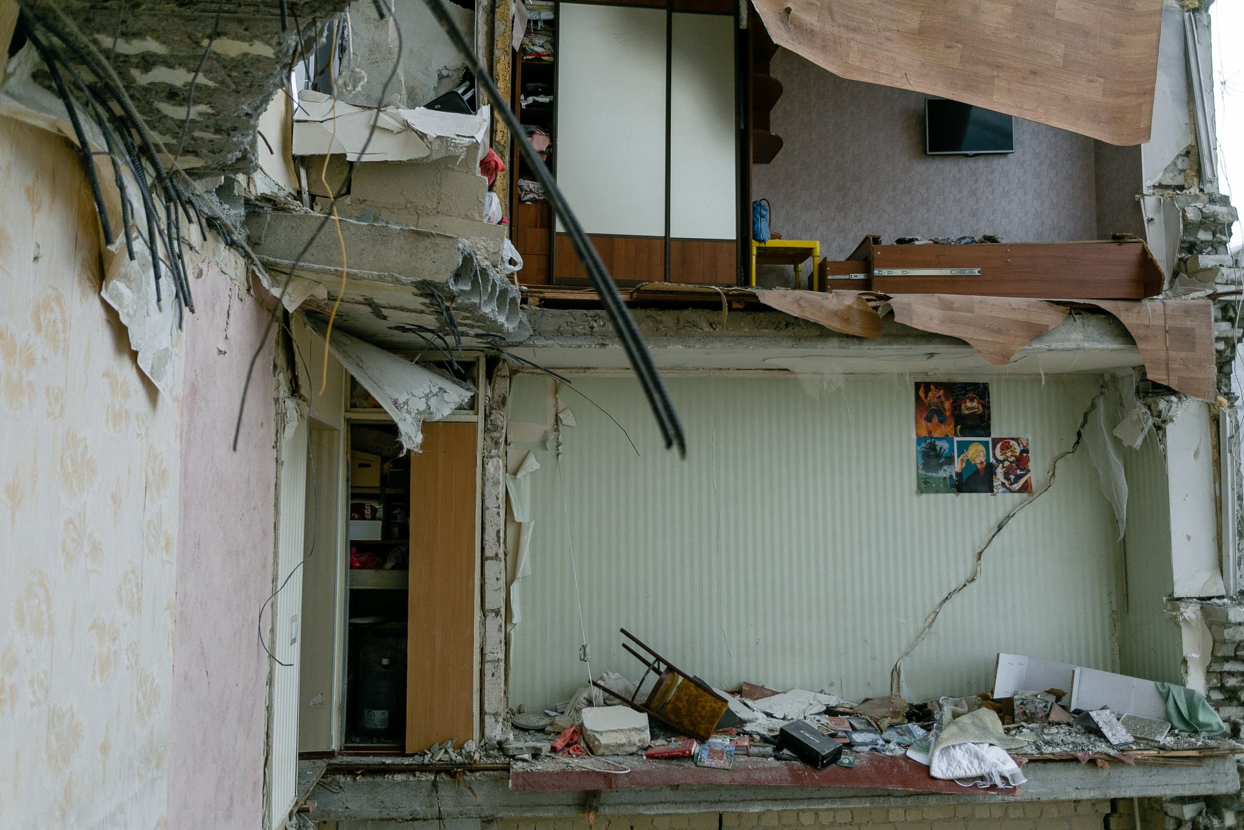 Разрушенная взрывом стена многоквартирного дома, обнажающая интерьер двух этажей с мебелью и личными вещами.