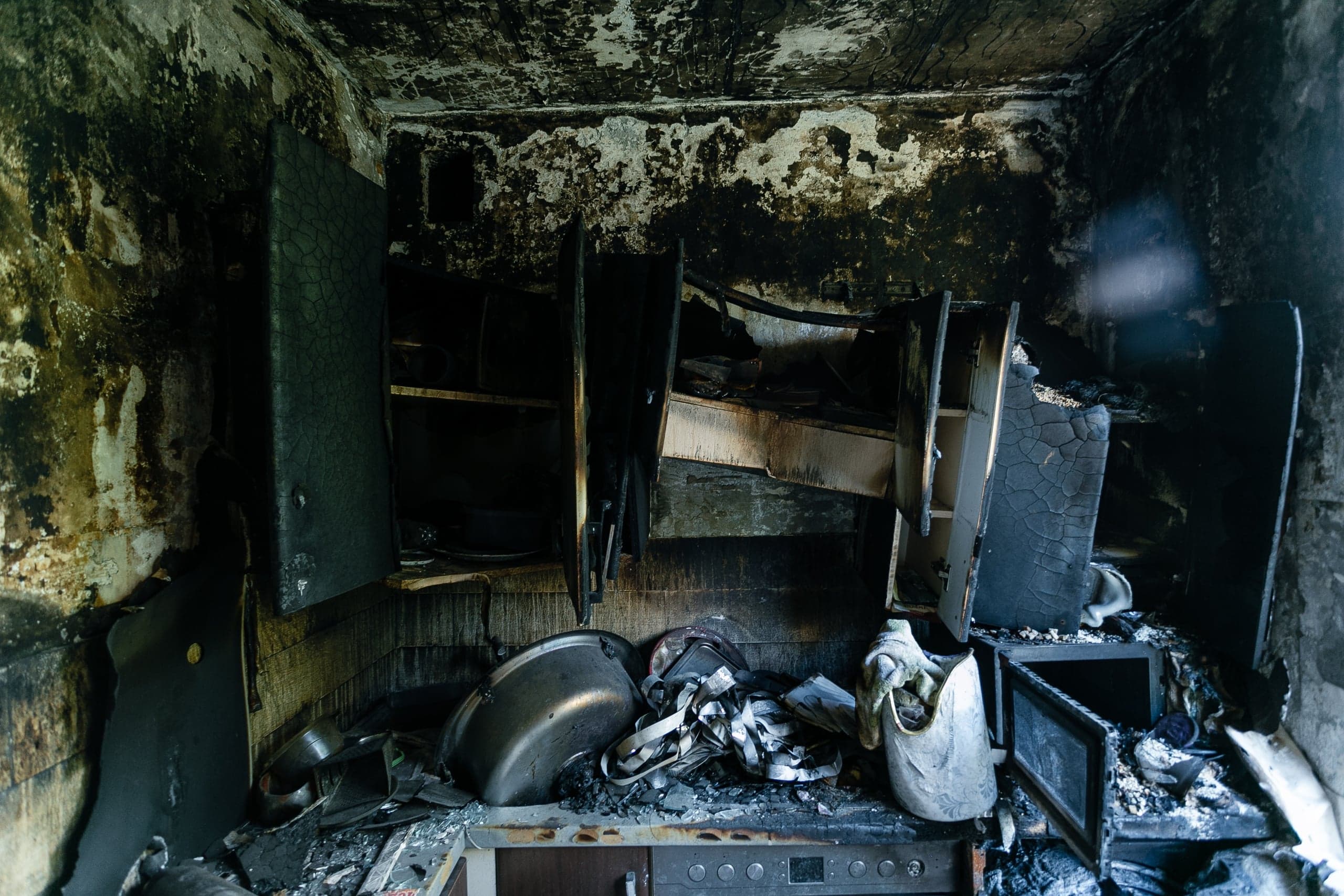 Сгоревший интерьер кухни: закопченные стены, разрушенные шкафы и обломки на столешнице.