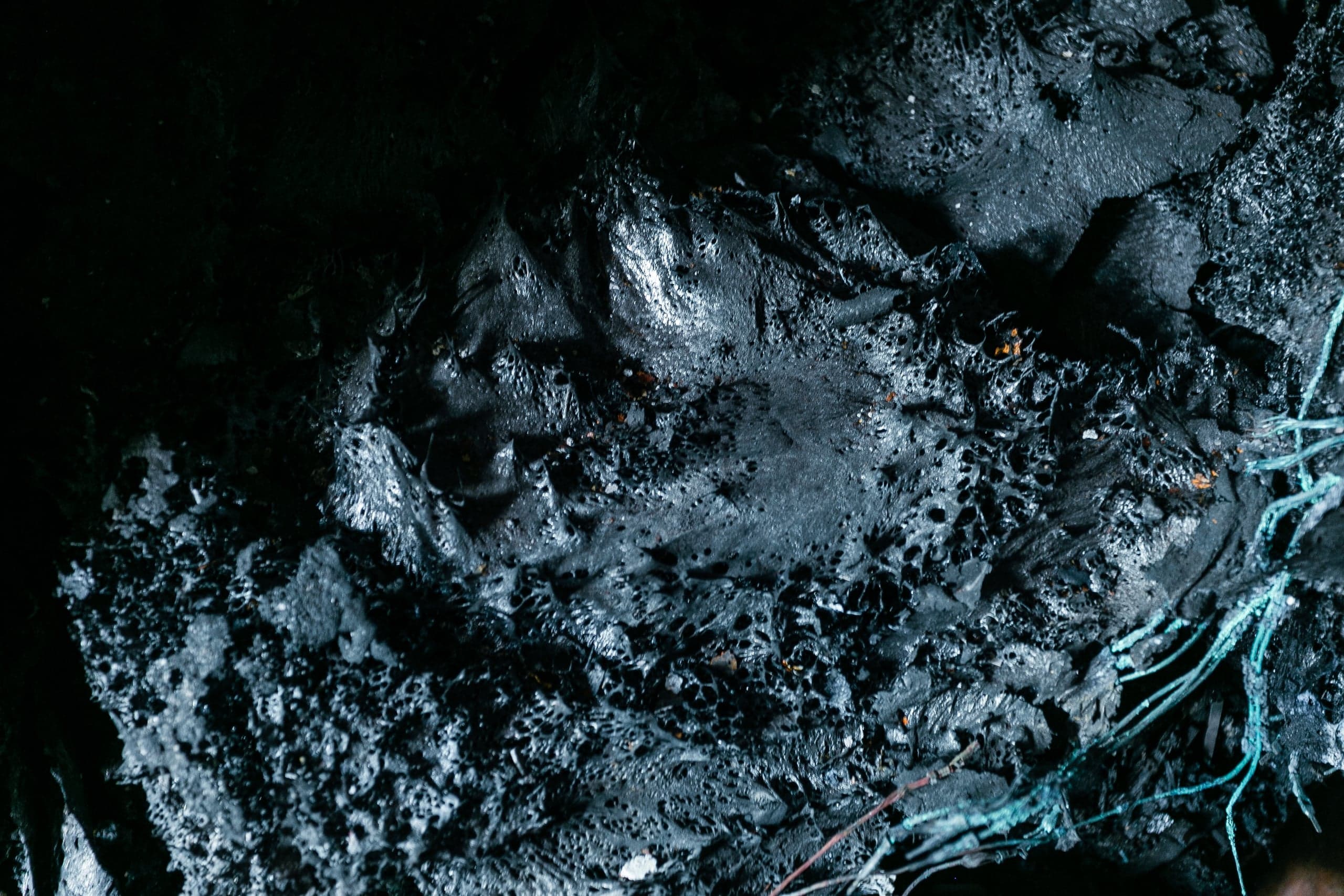 Темная текстура расплавленного обугленного материала с пористыми отверстиями и бирюзовыми проводами.