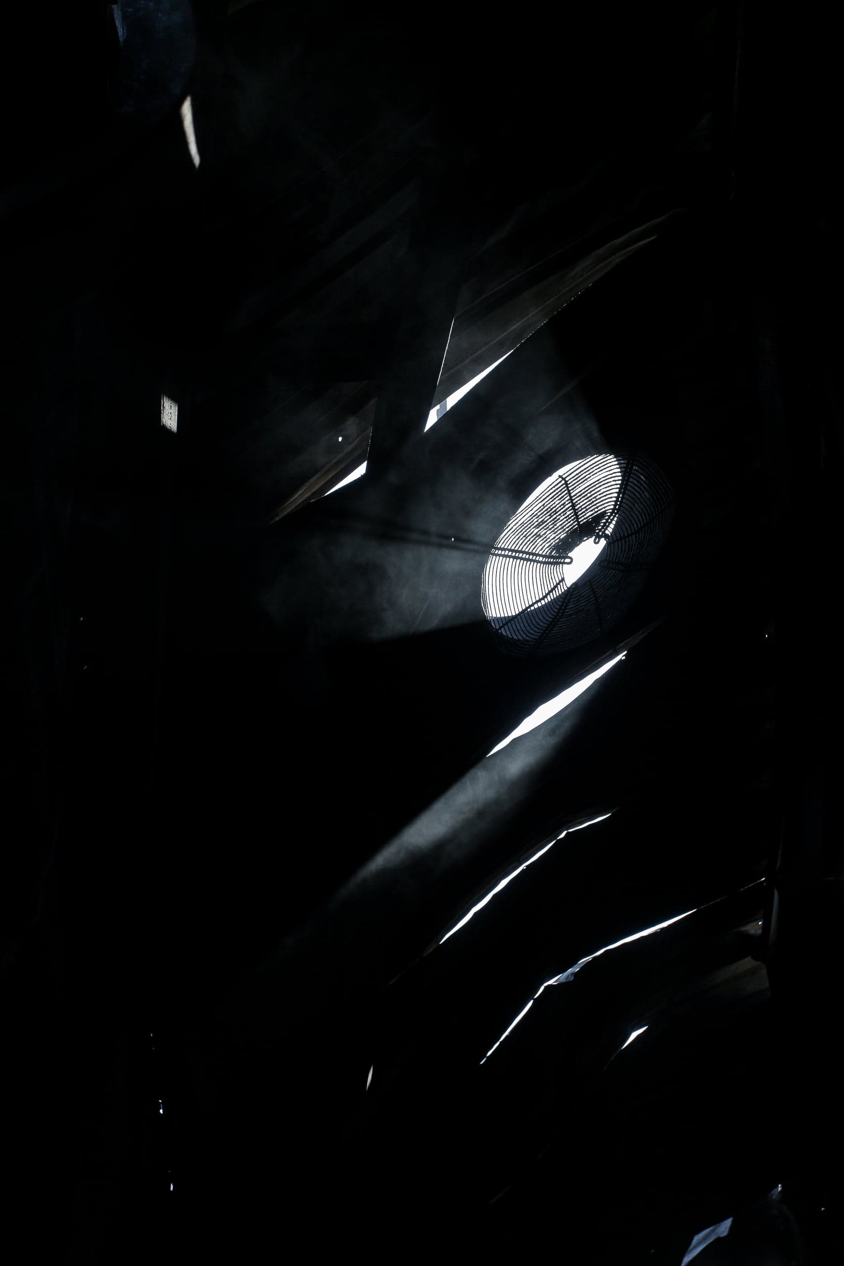 Лучи света и дым, проникающие через щели и вентилятор в темном помещении.