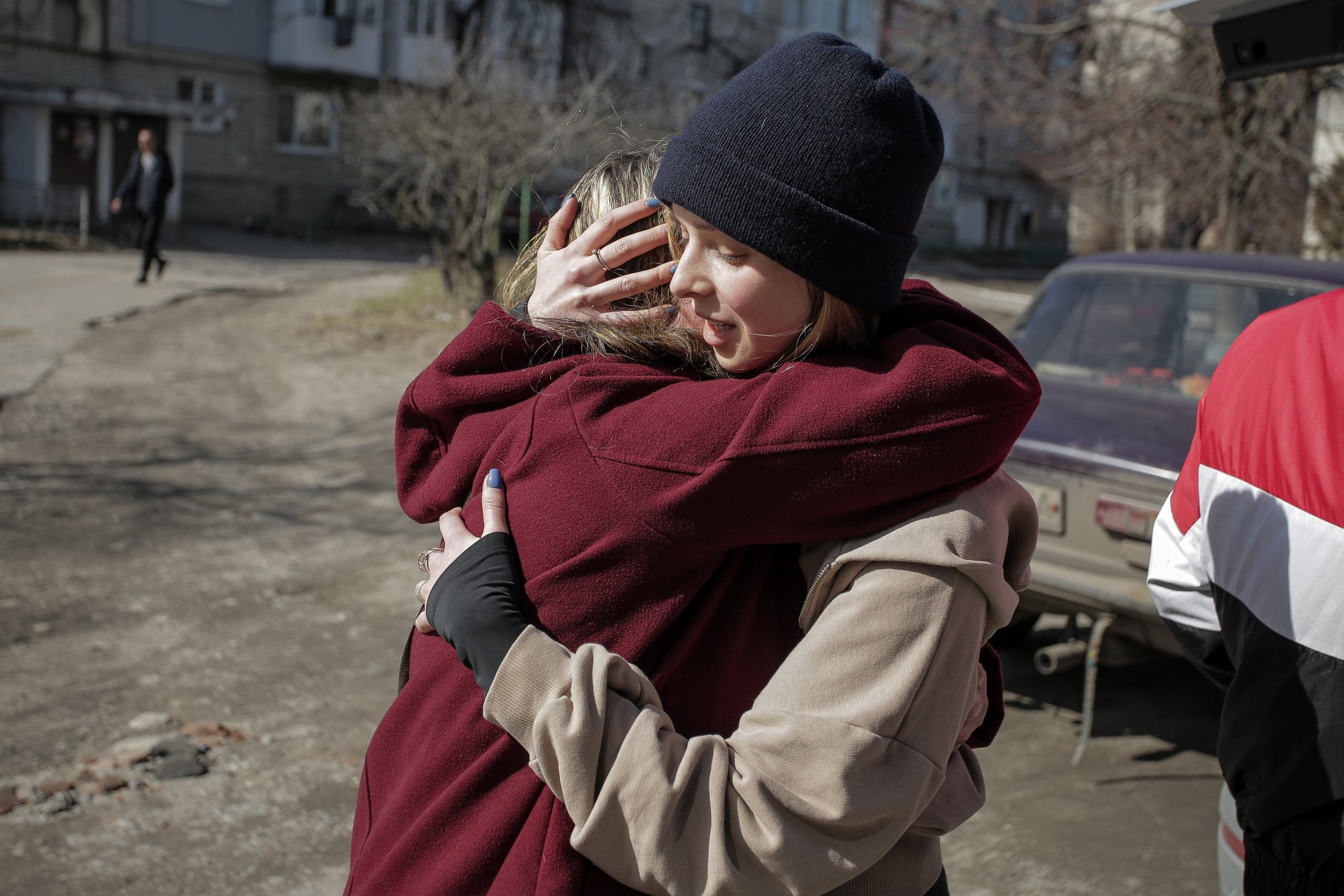 Крупный план: две женщины крепко обнимаются на улице перед жилыми домами.