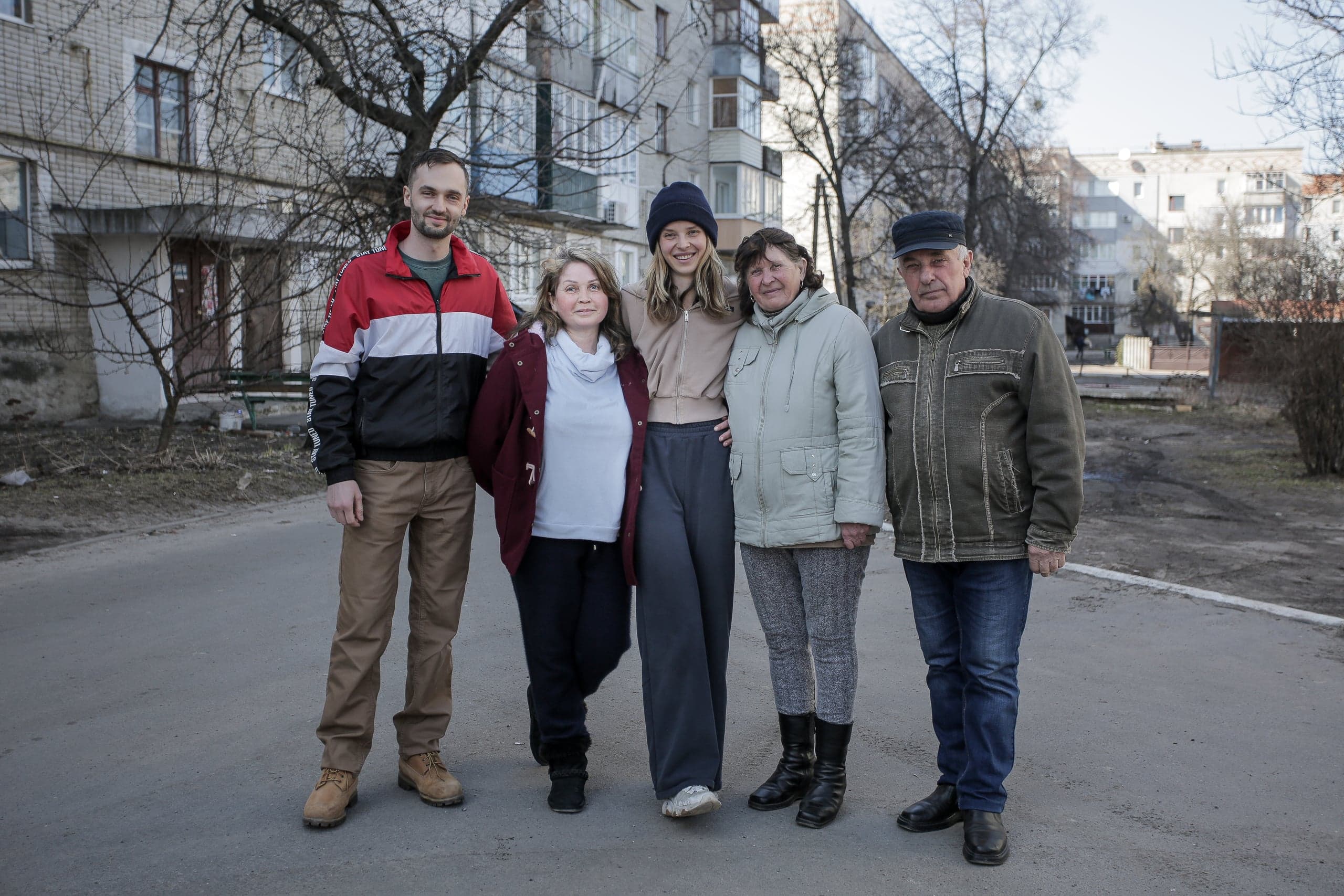 Групповой портрет пяти человек (двое мужчин, три женщины) на улице на фоне многоквартирных жилых домов.