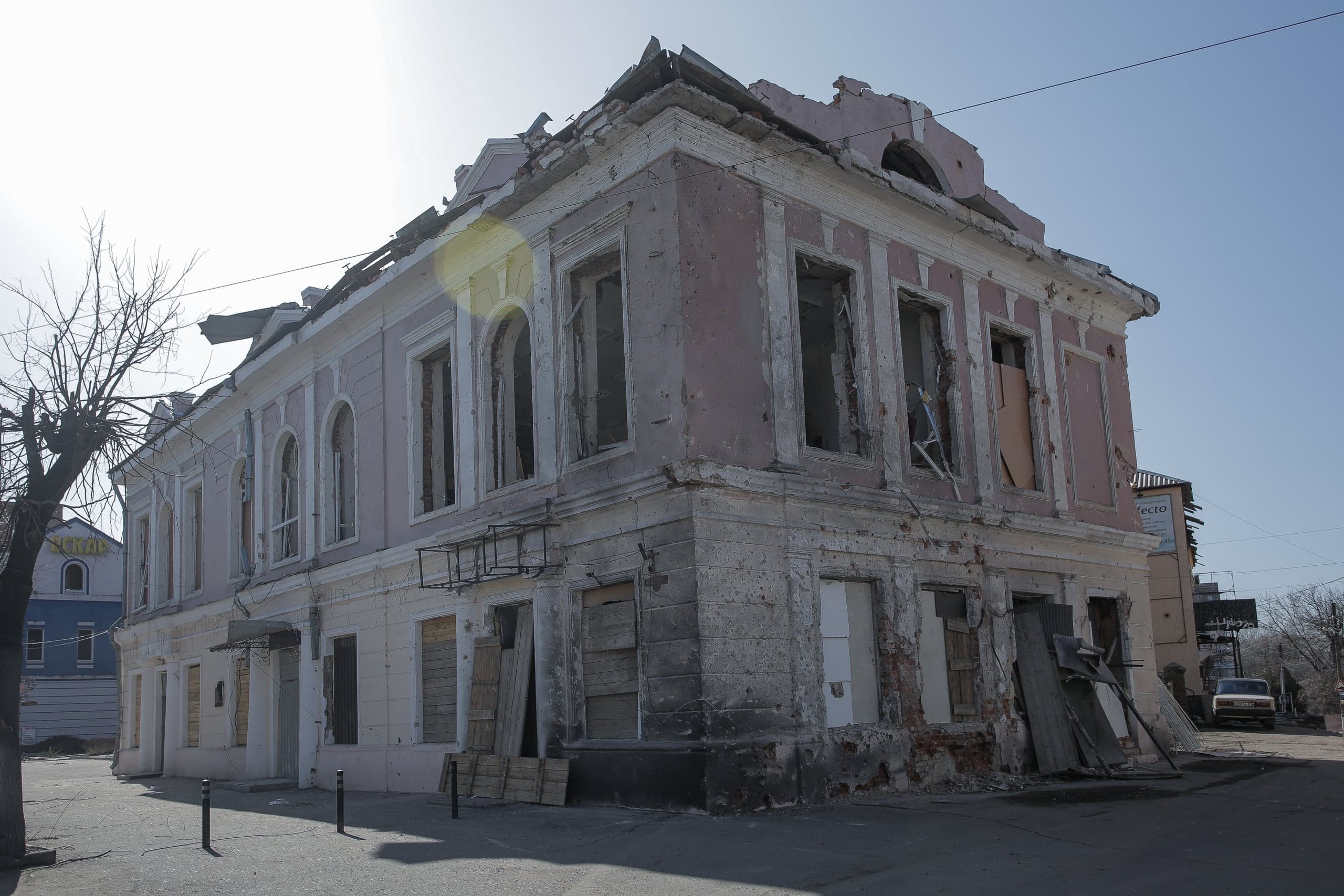 Сильно поврежденное двухэтажное здание с частично разрушенной крышей и выбитыми окнами. Фасад бледно-розового и белого цвета.