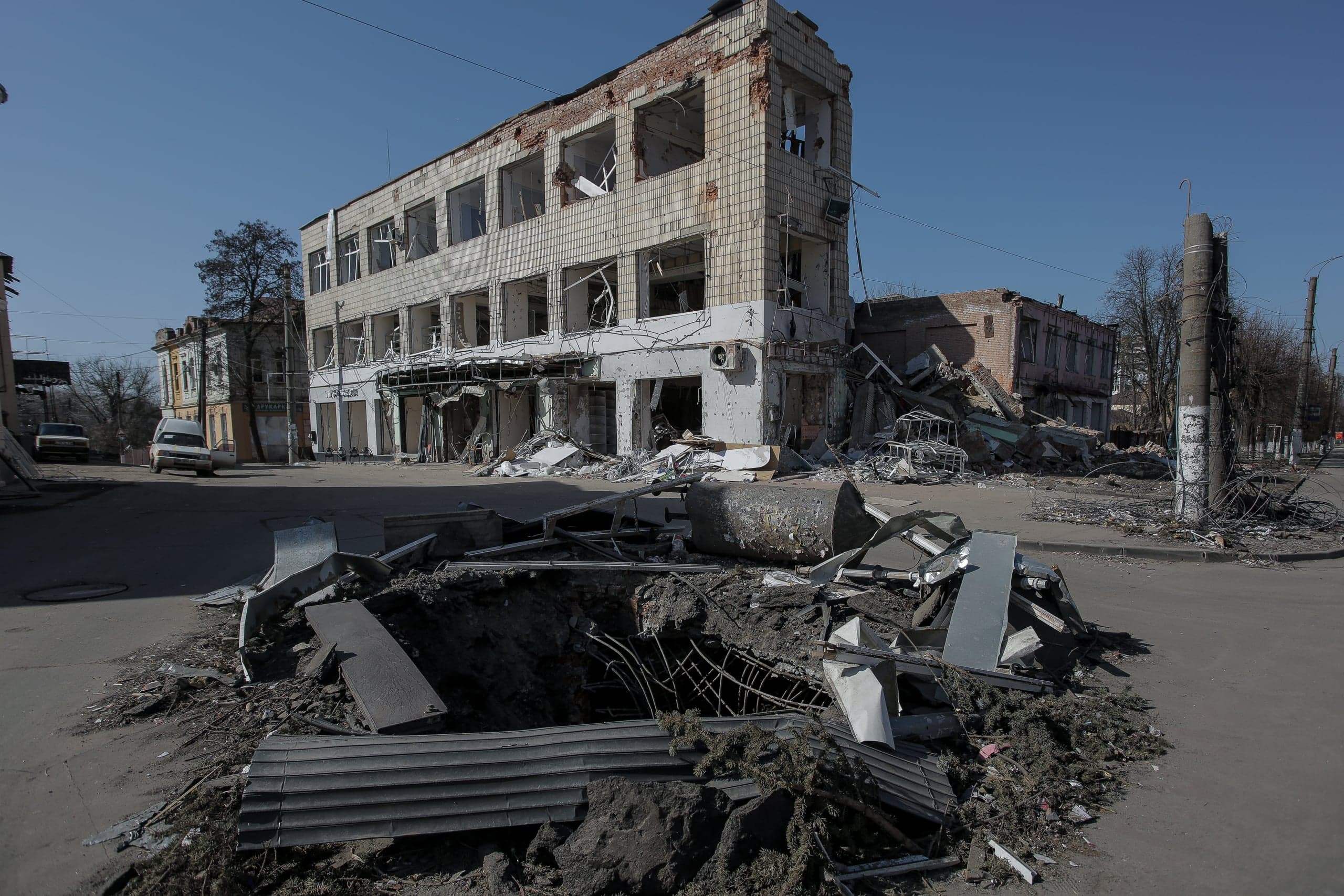 Сильно разрушенное трехэтажное здание и большая куча обломков с воронкой на городской улице.
