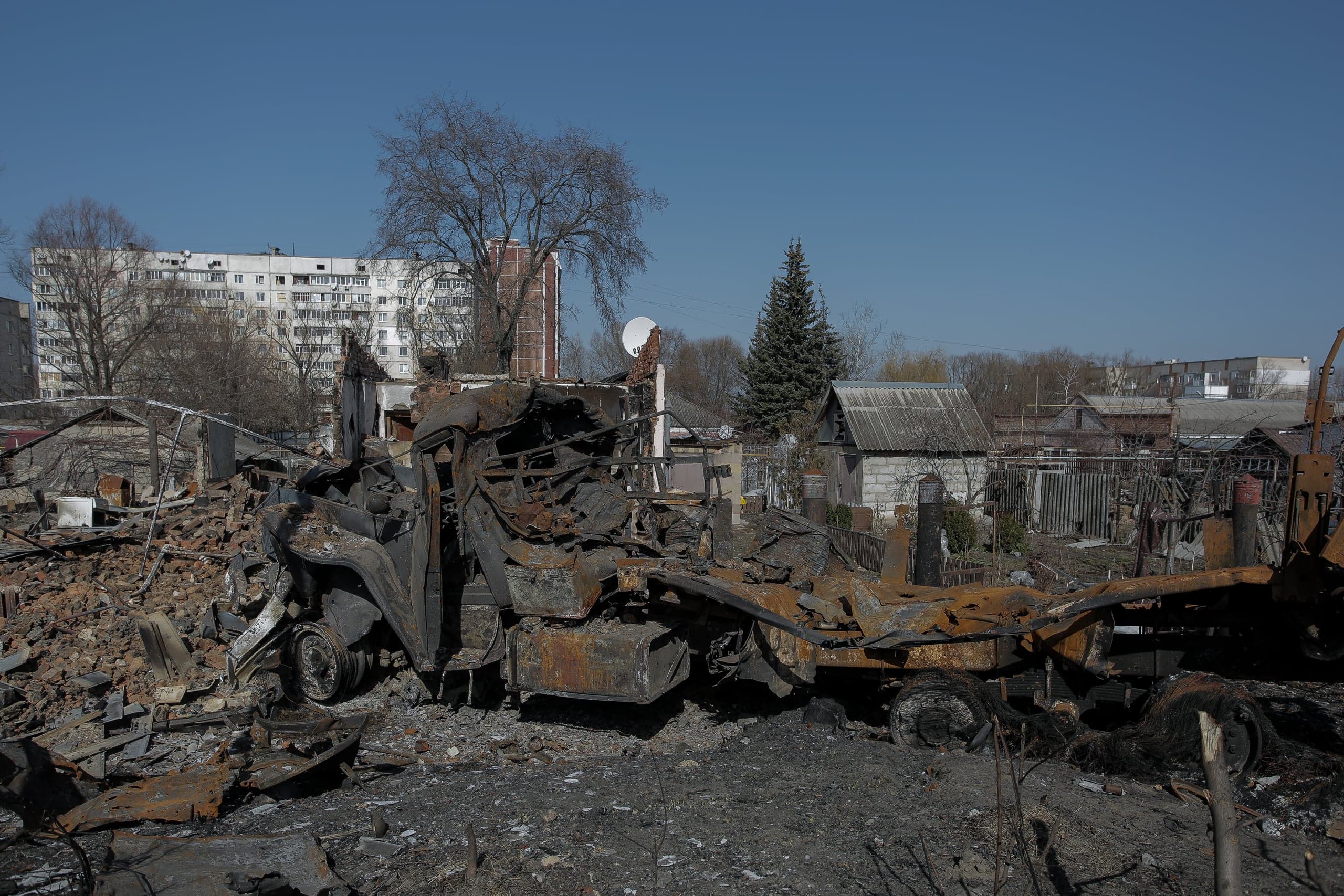 Сгоревшие руины и остов машины в частном секторе на фоне целого многоэтажного дома.