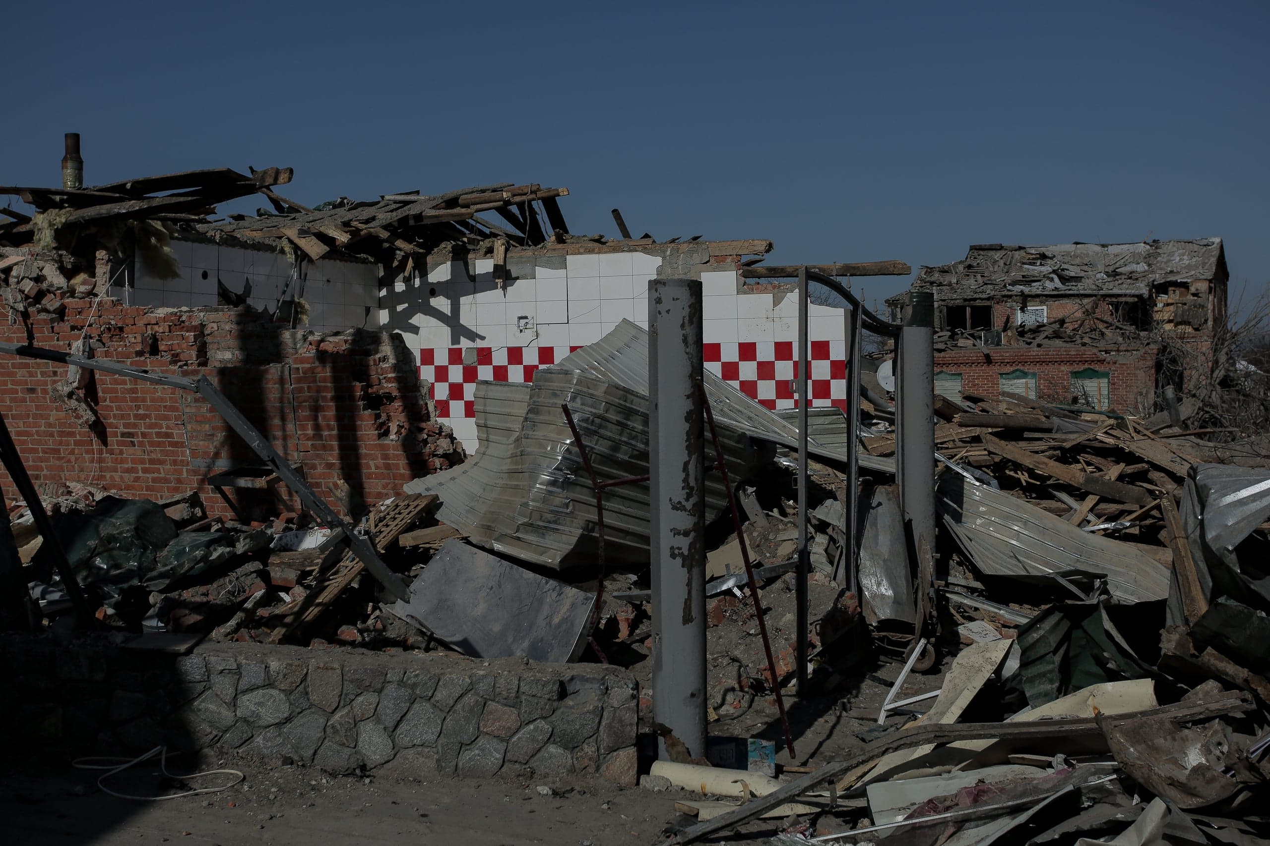 Руины здания, заваленные обломками, с уцелевшим фрагментом красно-белой плитки в клетку на стене.