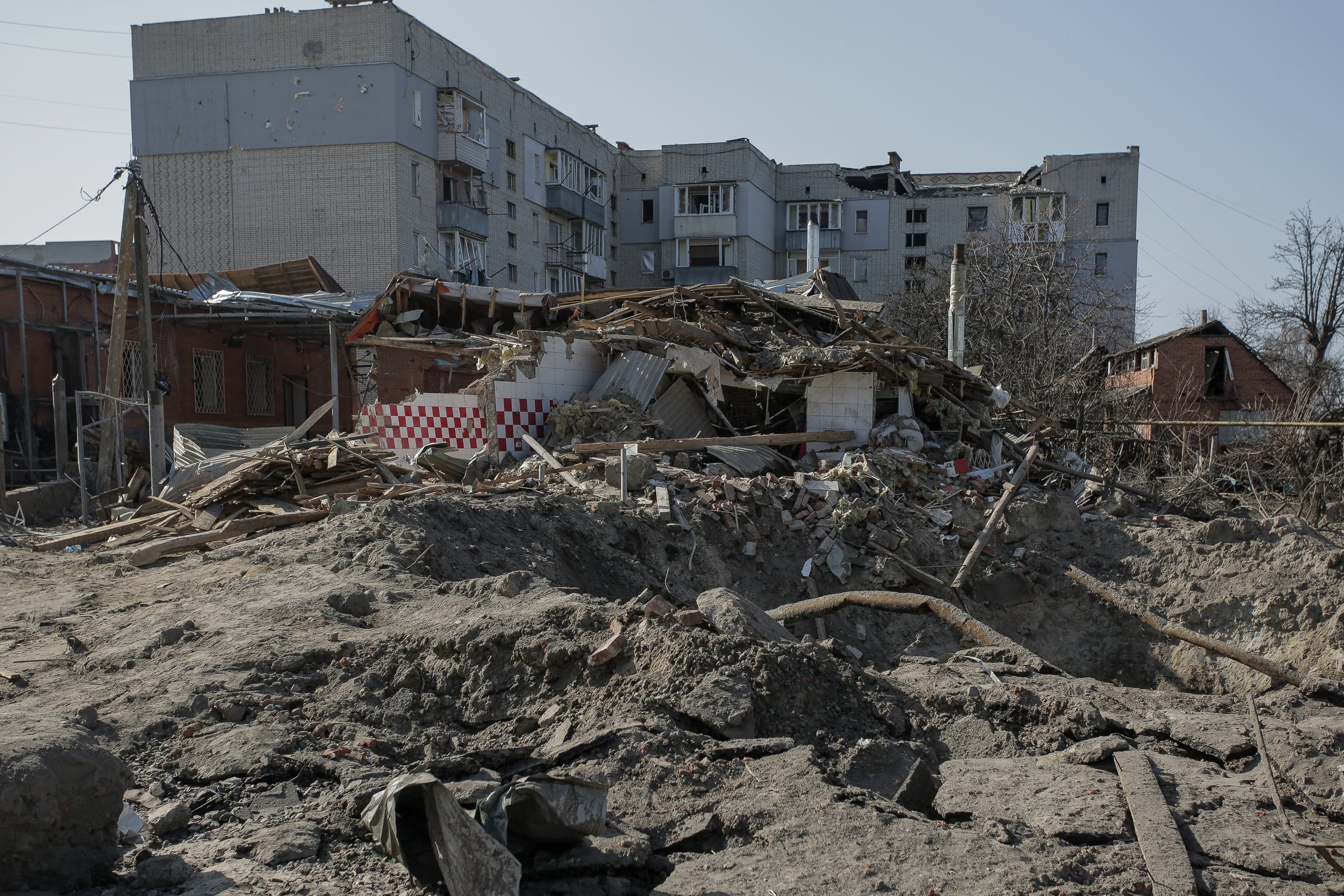 Руины зданий: горы обломков на фоне поврежденного многоэтажного жилого дома.