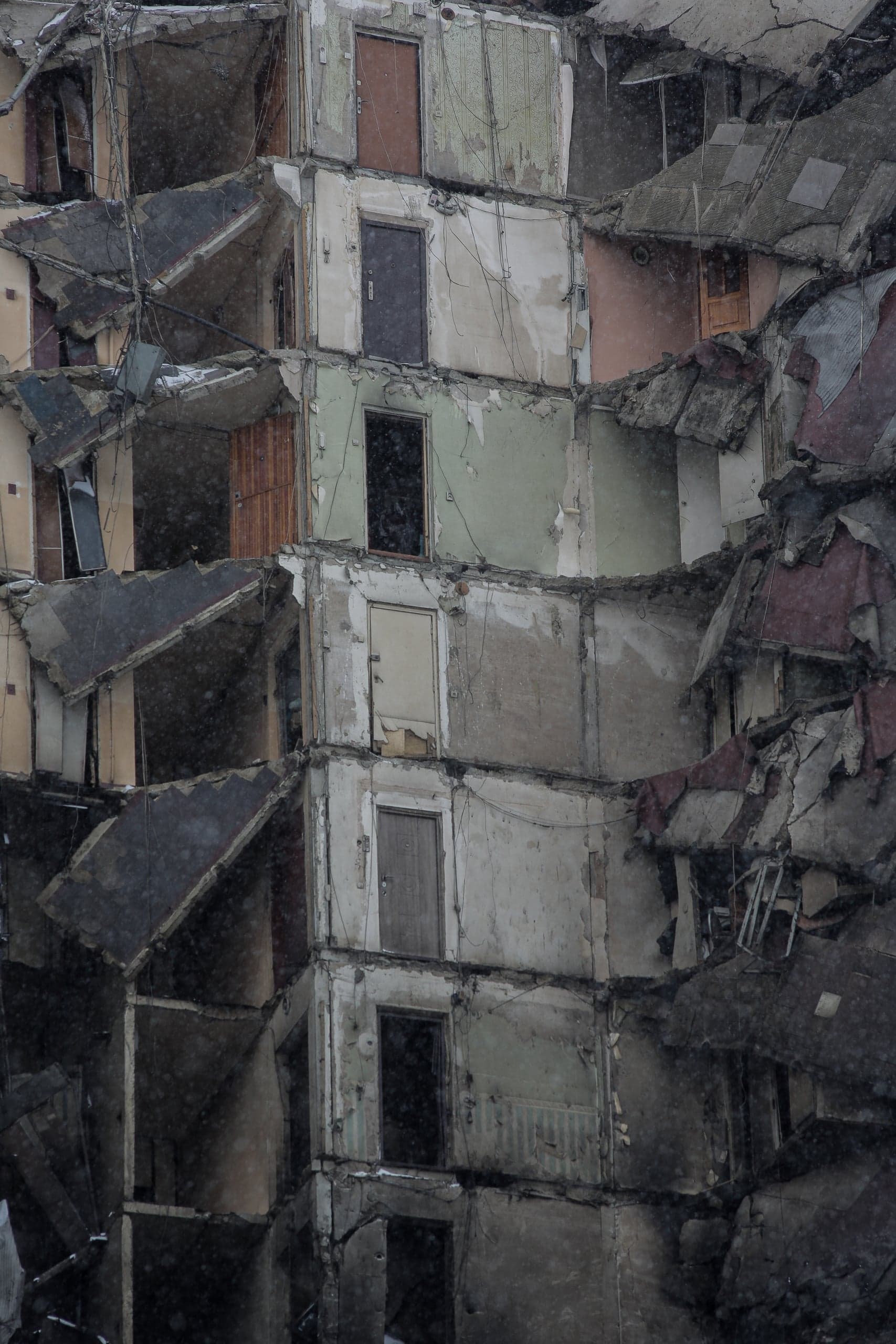 Разрушенное многоэтажное здание с обвалившимися стенами и рядами дверных проемов, снятое во время снегопада.