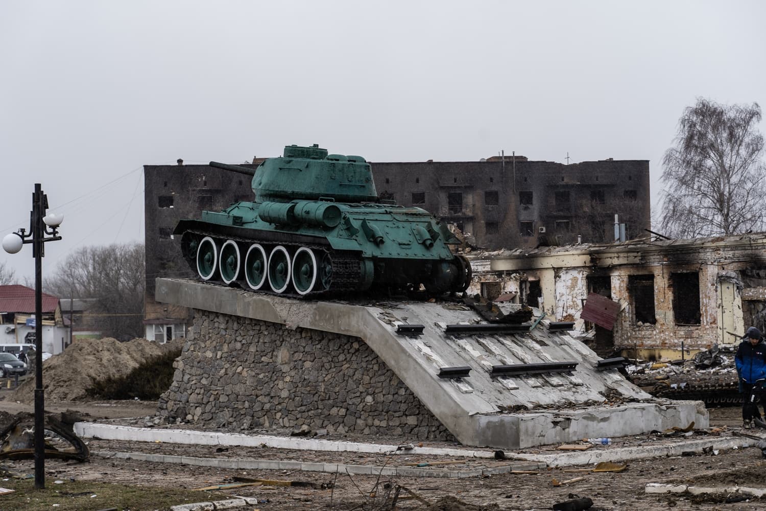 Памятник танку Т-34 на постаменте, окруженный сгоревшими и разрушенными зданиями.