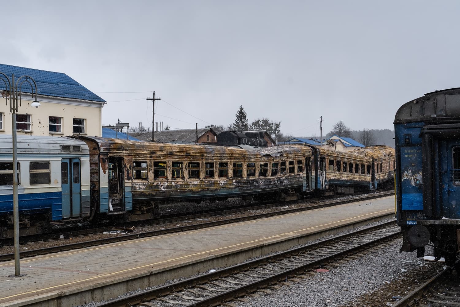 Обгоревшие и сильно поврежденные железнодорожные вагоны на путях перед зданием вокзала.