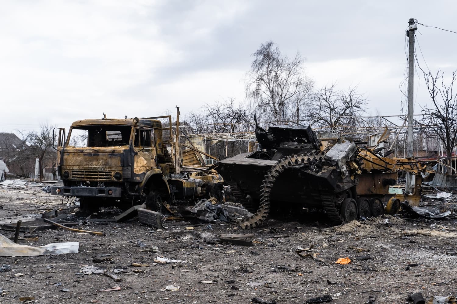 Обугленный военный грузовик и уничтоженная гусеничная бронемашина среди руин.