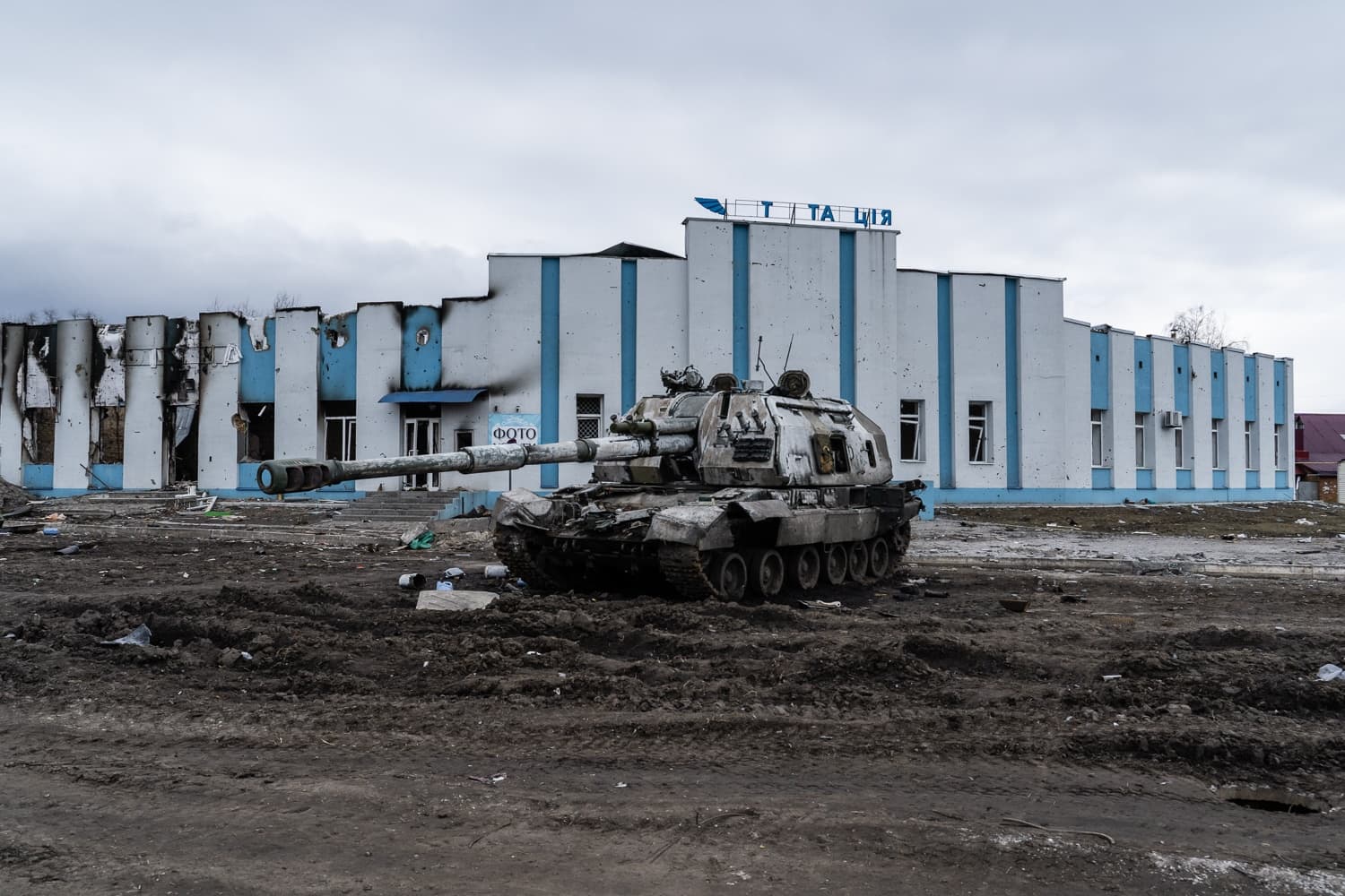 Сгоревшая бронетехника на фоне разрушенного здания с надписями "Т А Ц І Я" и "ФОТО".
