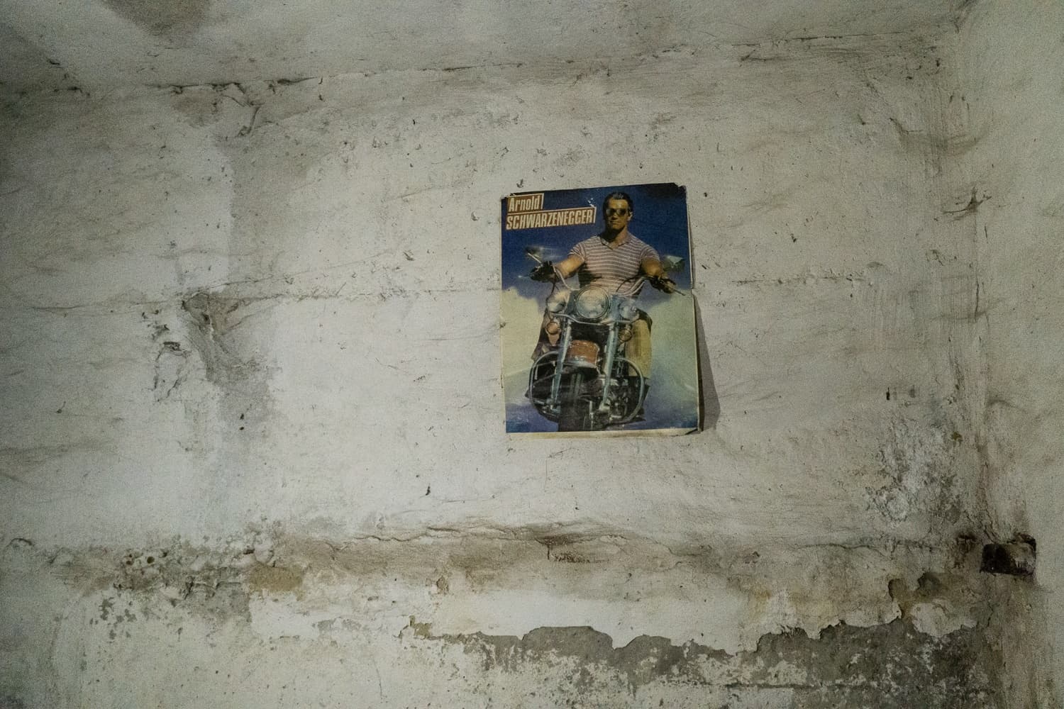 Постер с Арнольдом Шварценеггером на мотоцикле ("Arnold SCHWARZENEGGER") на обшарпанной бетонной стене.