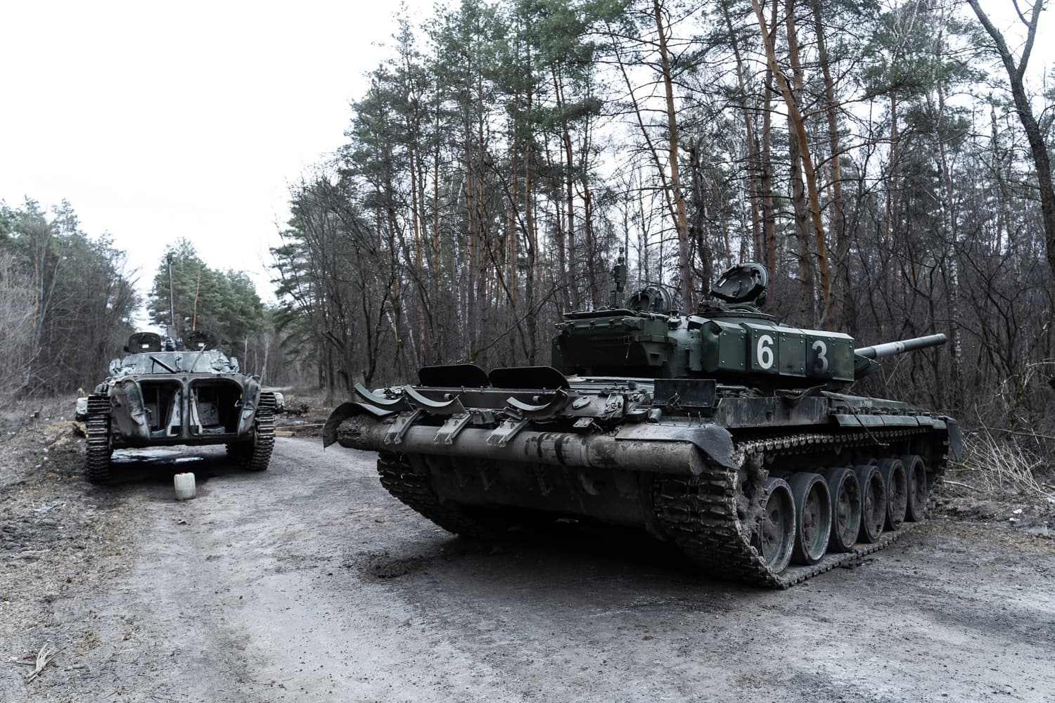 Подбитый танк Т-72 с маркировкой "63" и поврежденная БМП на лесной дороге.