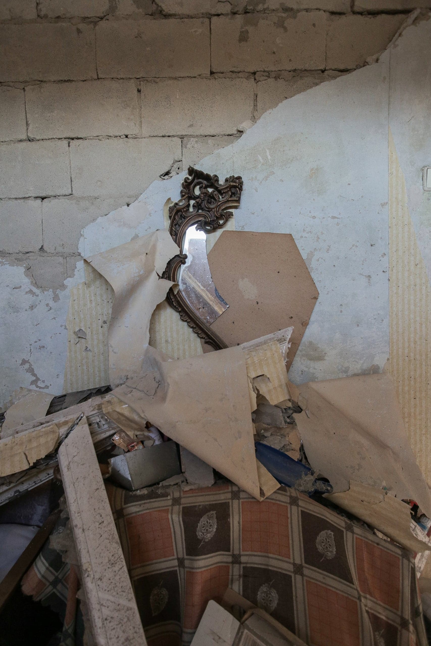 Shattered ornate mirror amidst строительного мусора, обвалившихся обоев и обломков мебели в разрушенном помещении.