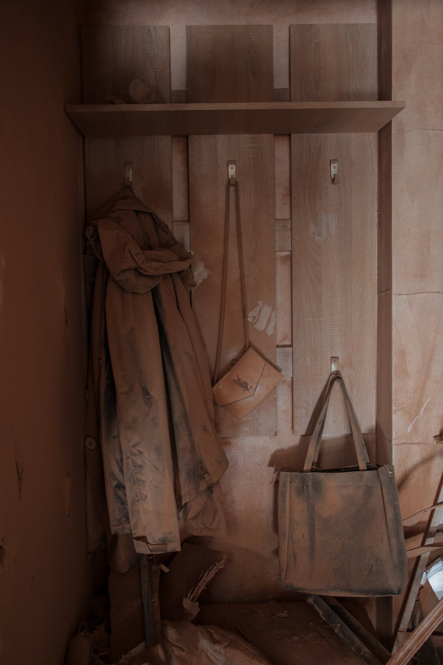 Шкафчик с одеждой и сумками, покрытыми толстым слоем коричневой вулканической пыли.