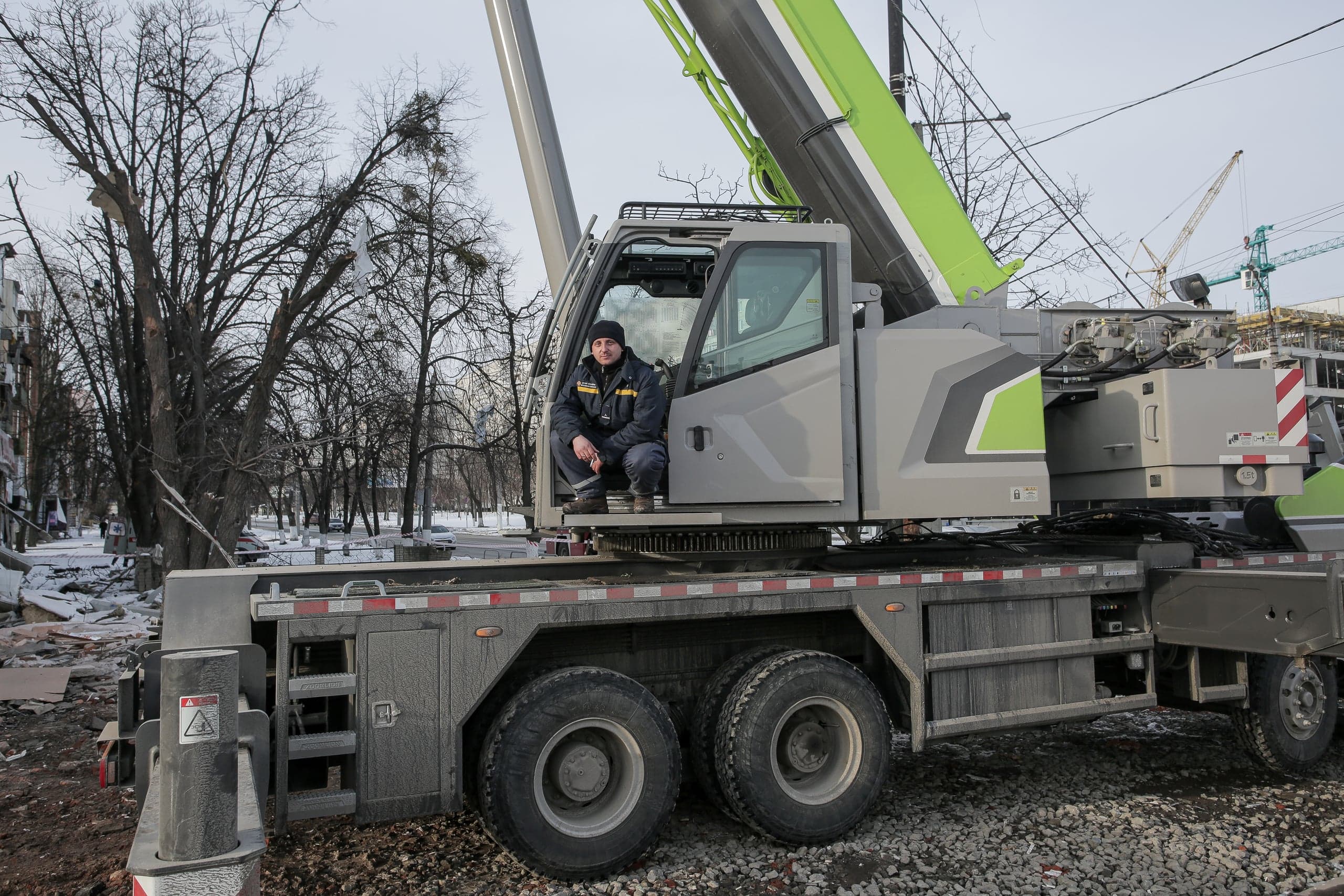 Мужчина сидит, высунувшись из водительской кабины большого строительного крана