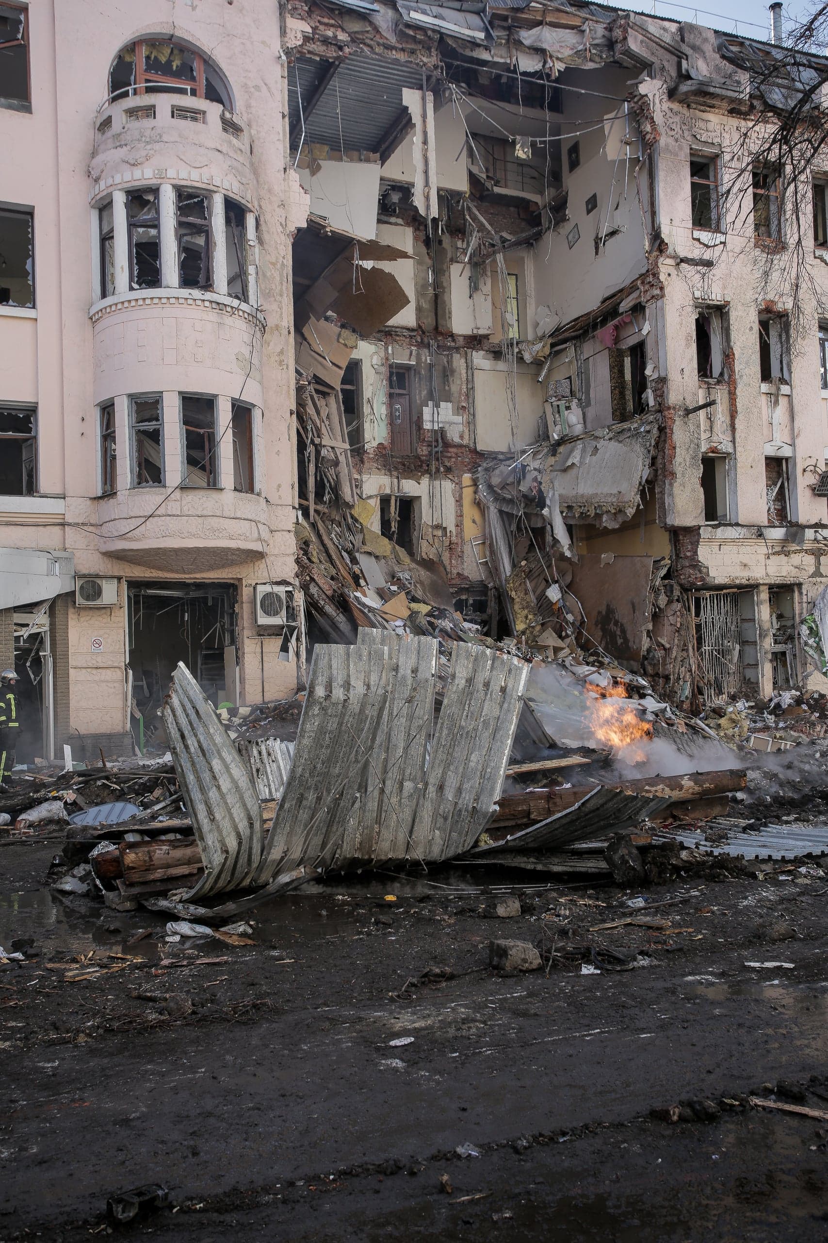 Разрушенный взрывом многоэтажный дом, обломки на земле и очаг возгорания.
