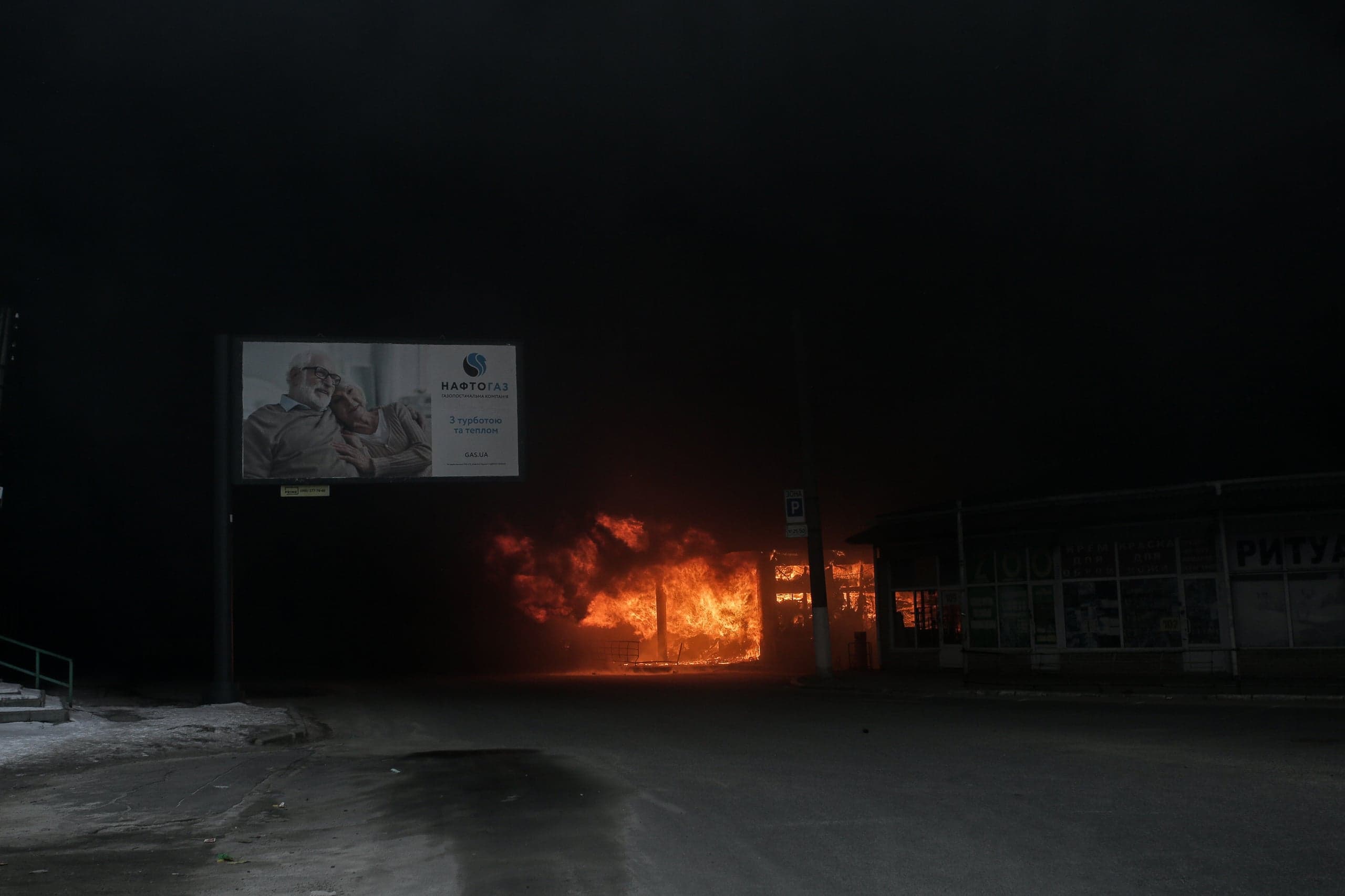 Ночью здание на улице охвачено сильным огнем. Слева рекламный щит "НАФТОГАЗ" с надписью "З турботою та теплом". На темном здании справа видна часть надписи "РИТУА".