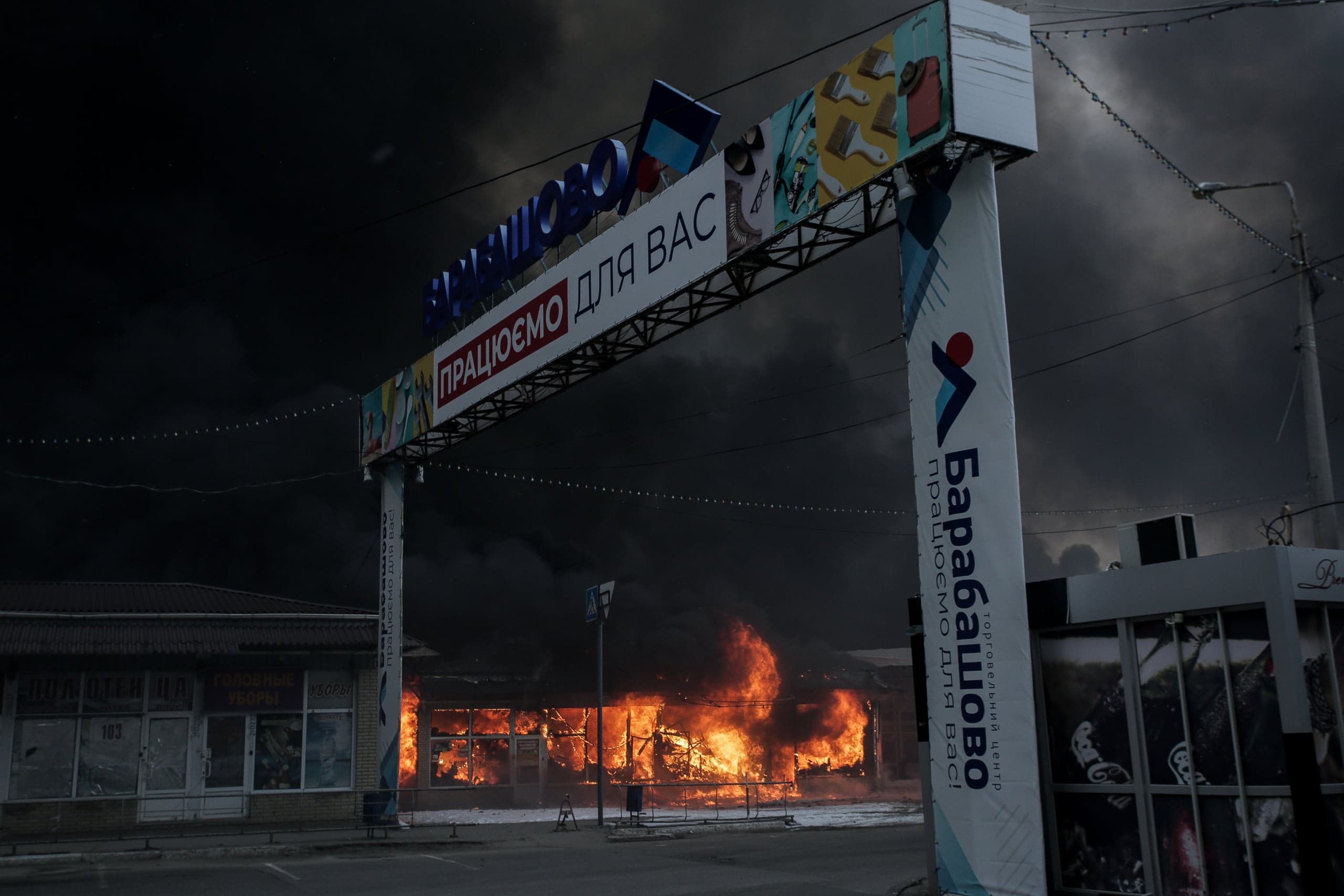 Здание торгового центра в огне под въездной аркой "БАРАБАШОВО". На арке также написано "ПРАЦЮЄМО ДЛЯ ВАС".