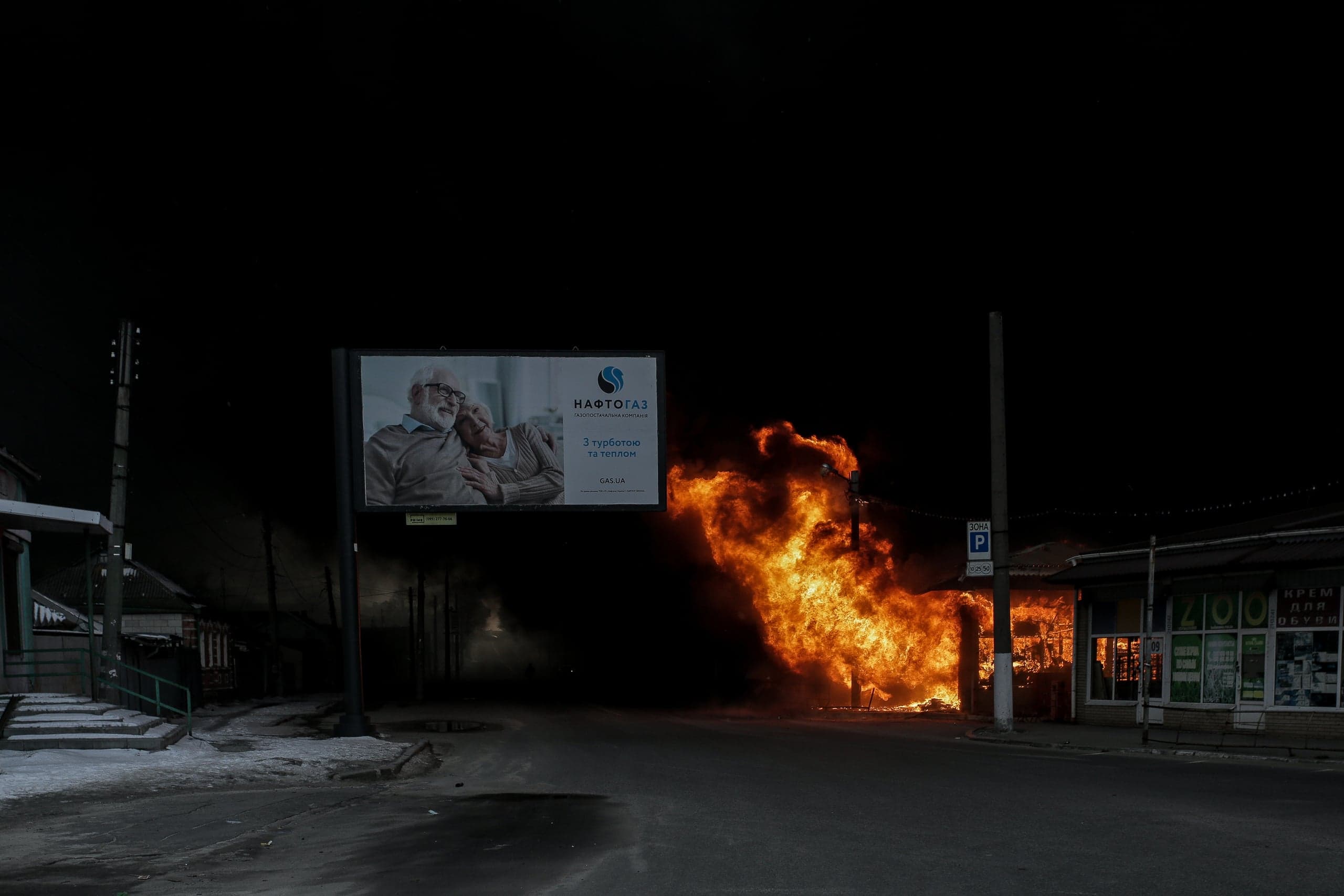 Ночь. Здание охвачено сильным пожаром на городской улице. Рядом стоит билборд "НАФТОГАЗ" с изображением пожилой пары и текстом "З турботою та теплом".