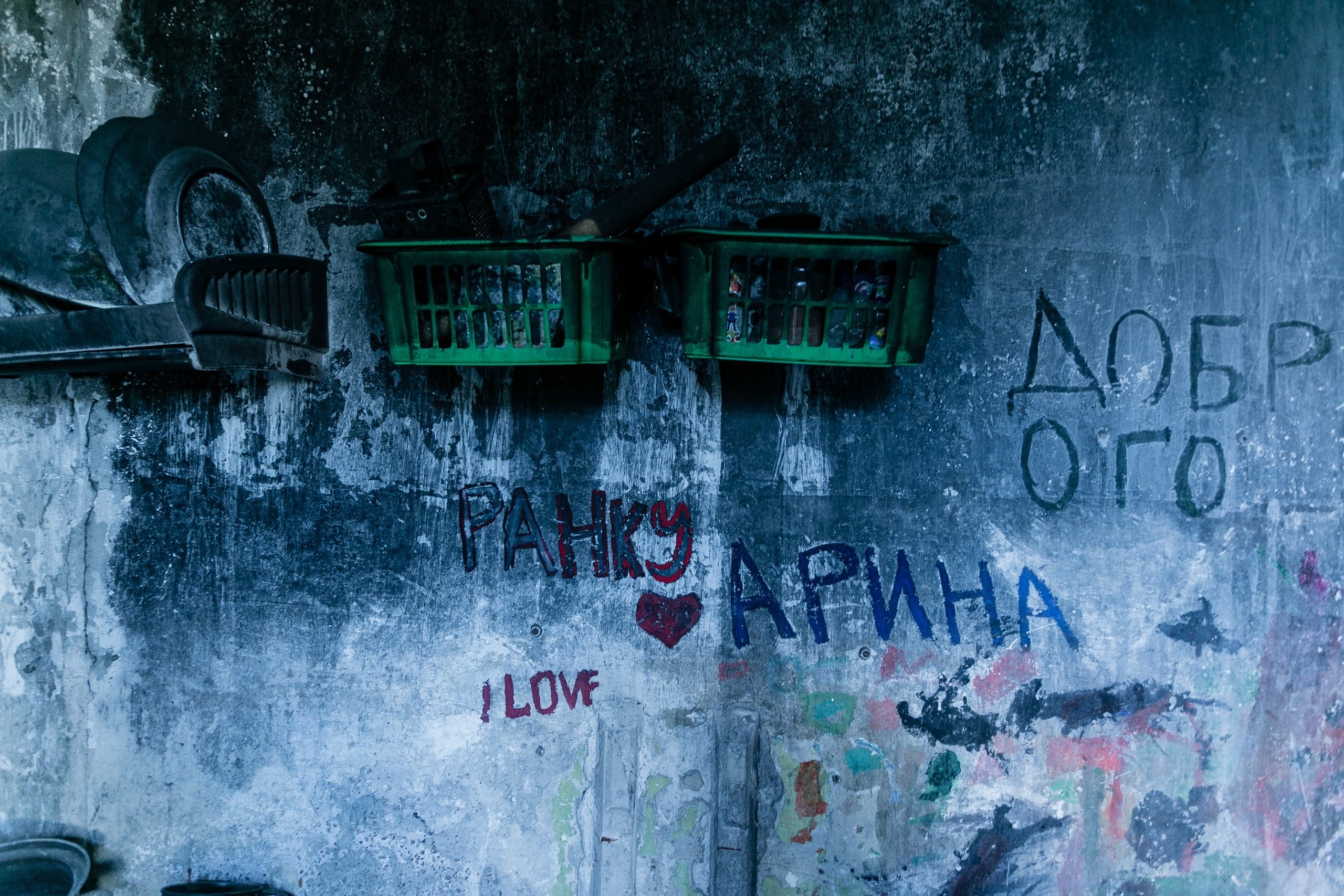 Темная, текстурированная стена с двумя зелеными корзинами и стопкой посуды. Граффити: "РАНКУ АРИНА", "I LOVE", "ДОБР ОГО".