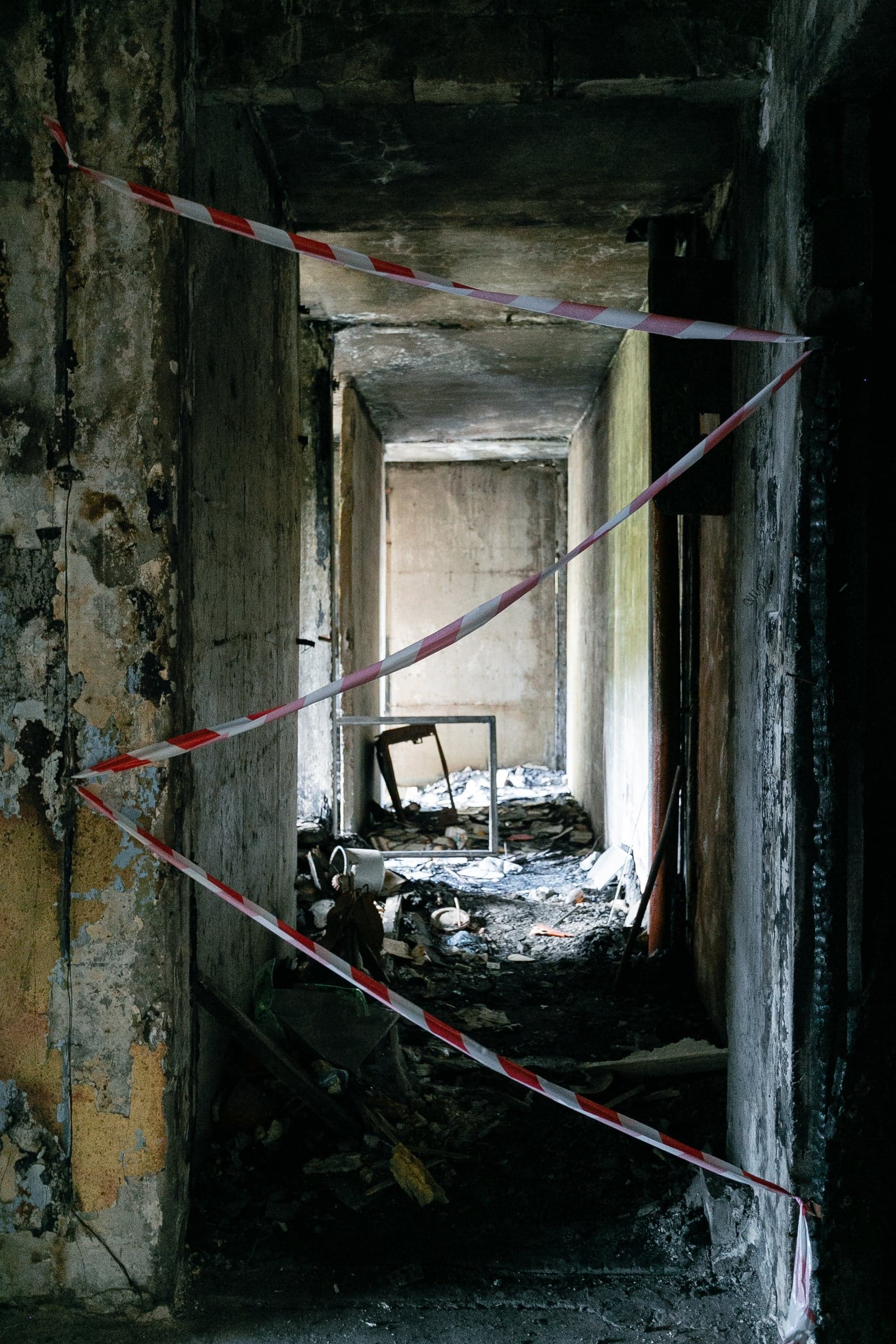 Обугленный коридор разрушенного здания, перегороженный красно-белой оградительной лентой.