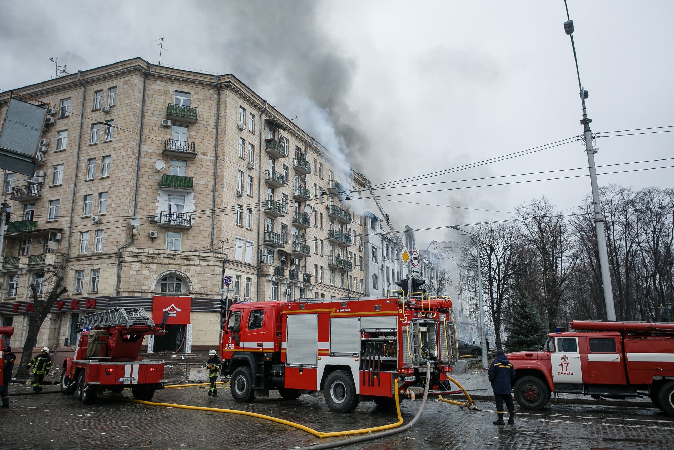 Пожарные тушат возгорание в многоэтажном здании. Из верхних этажей идет густой дым. На пожарной машине виден текст "ХАРКІВ 17".