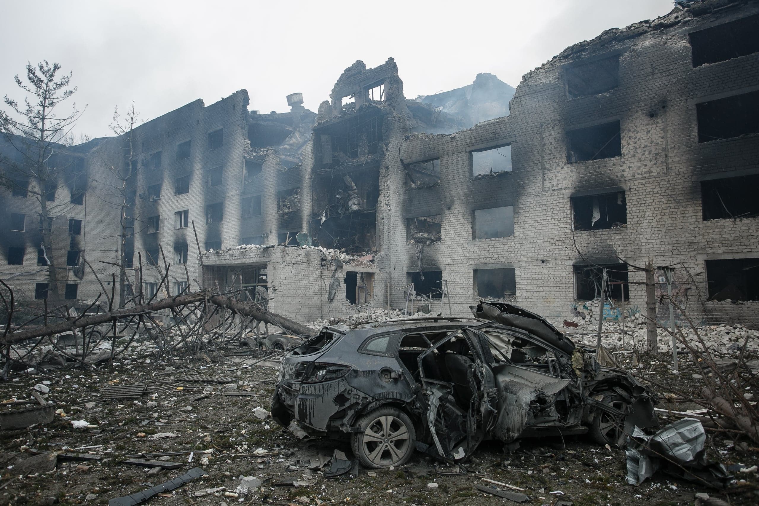 Сильно поврежденное обгоревшее здание и разбитый автомобиль среди обломков.