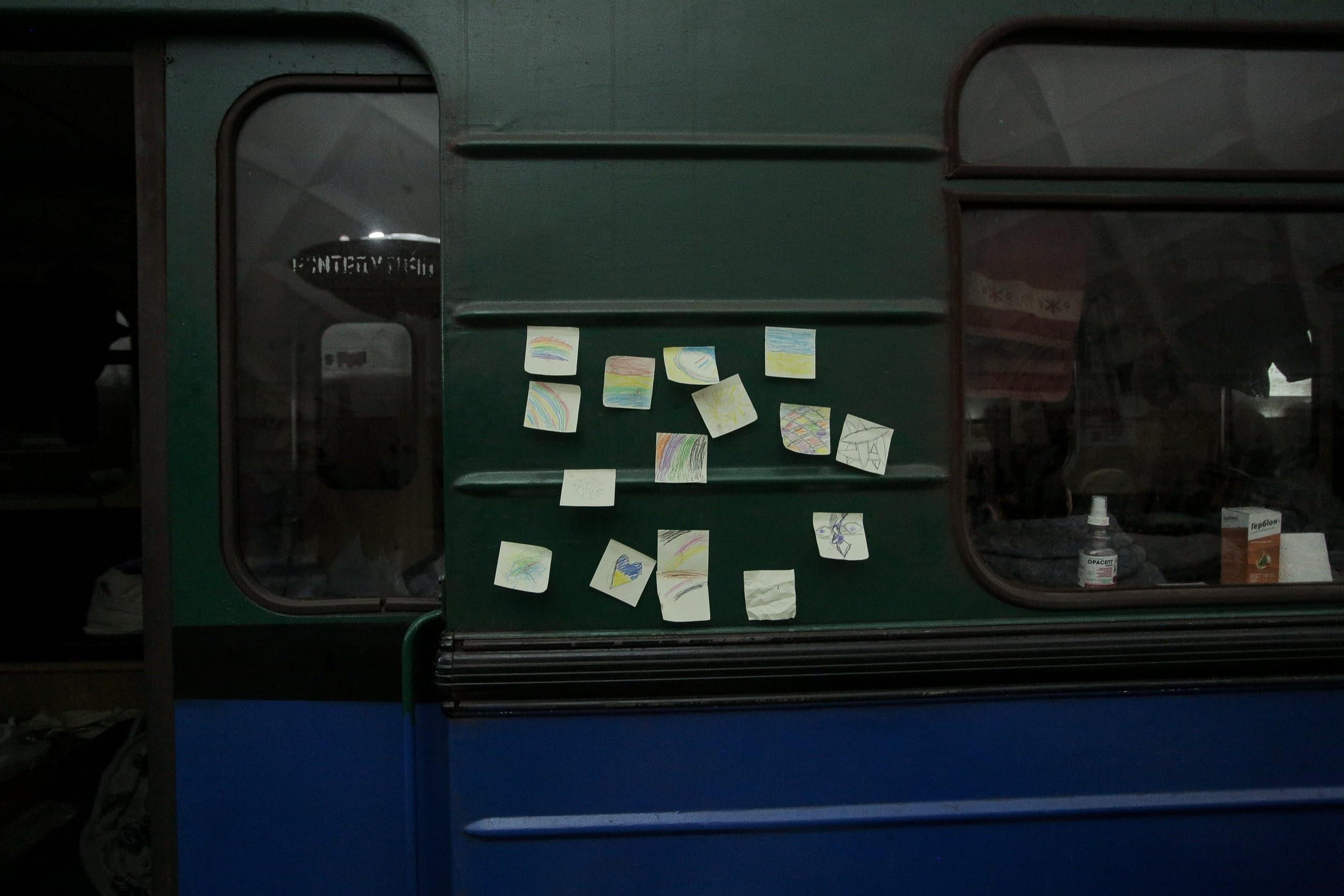 Панель вагона метро (зеленый верх, синий низ) с окнами и десятком детских рисунков на стикерах.