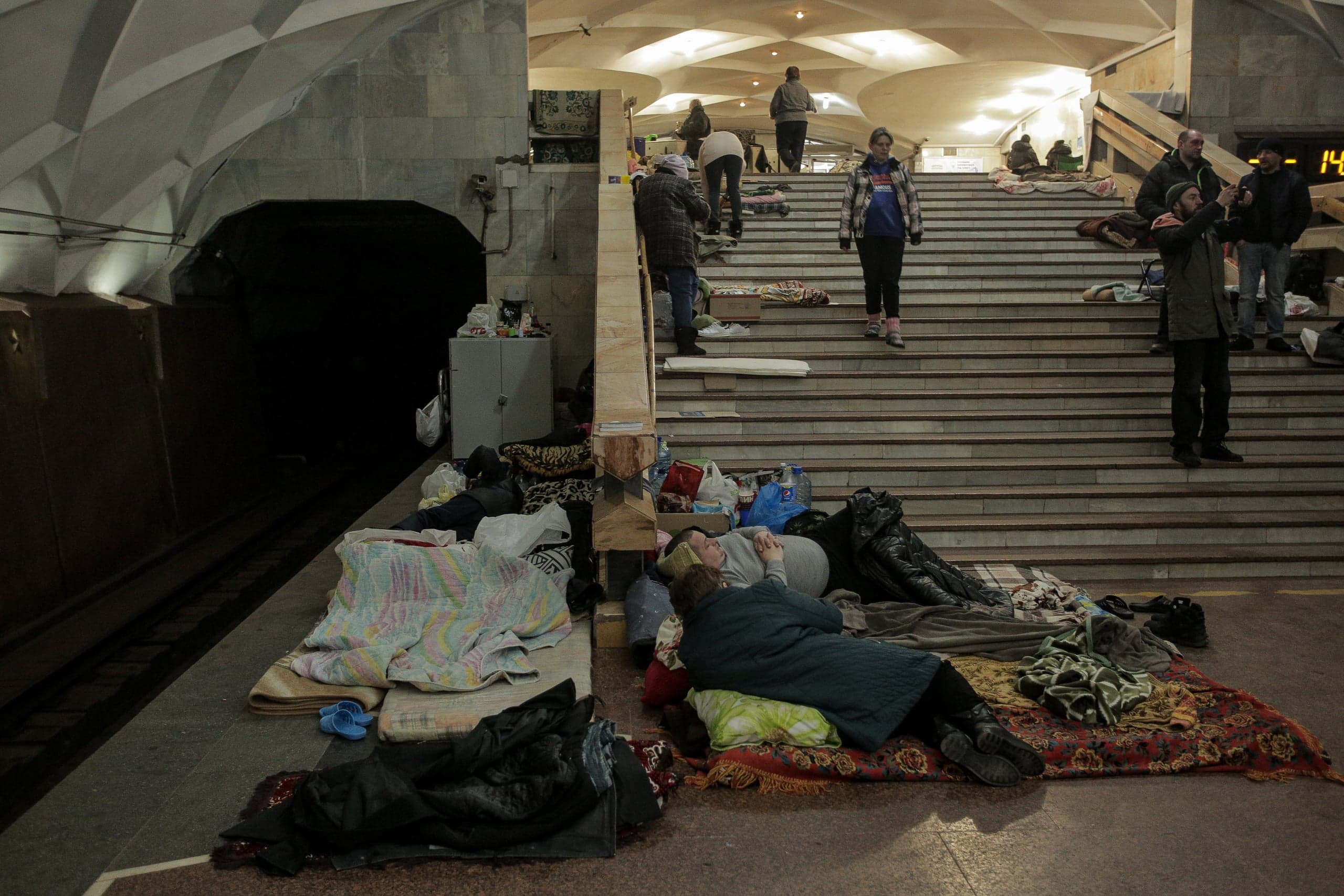 Люди укрываются на платформе и лестнице станции метро. На полу и ступенях лежат матрасы, одеяла и личные вещи.