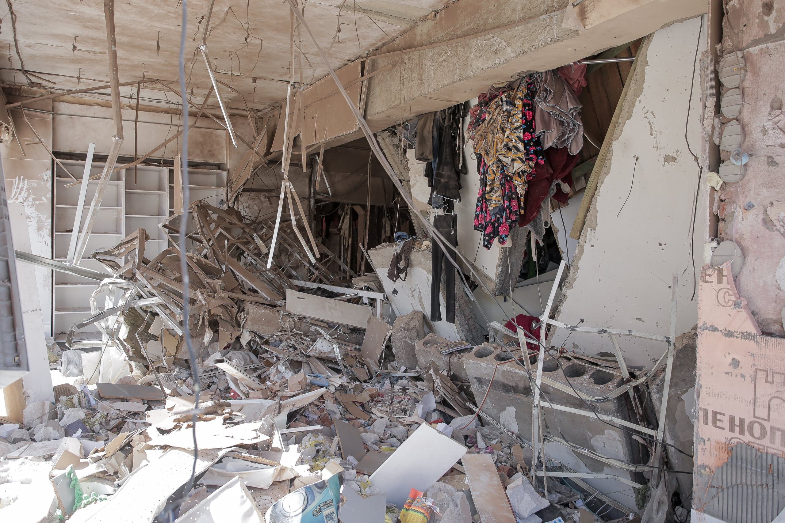 Сильно разрушенное внутреннее помещение, заваленное строительным мусором и обломками. Над завалами висит одежда.