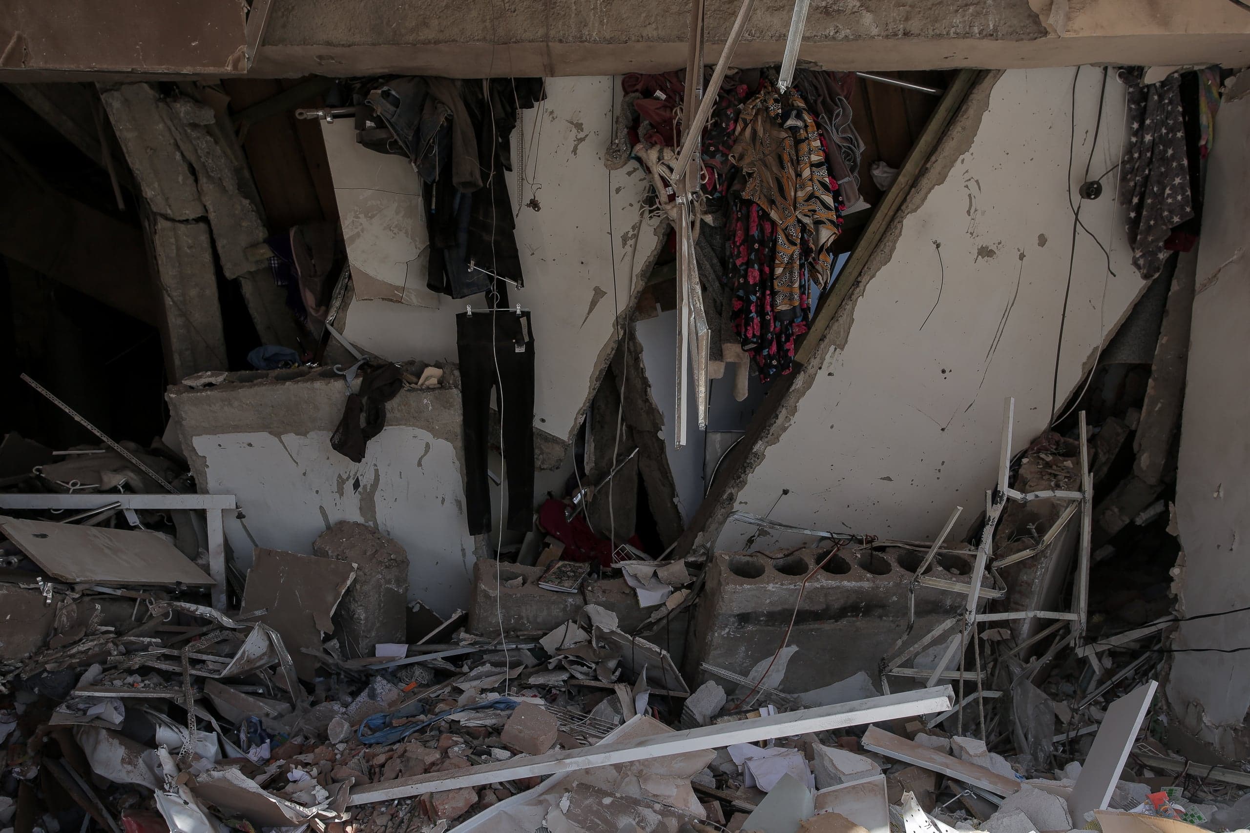 Разрушенный интерьер здания после обрушения, груда обломков и висящая на поврежденных стенах одежда.