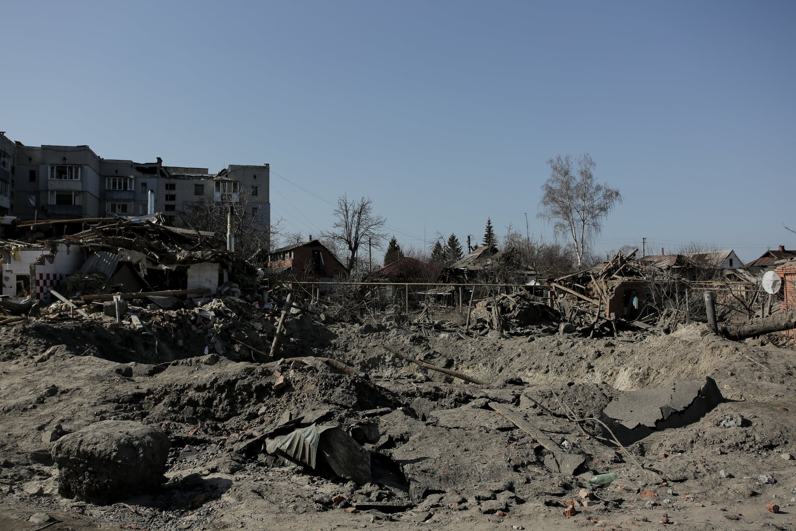 Sомные и разрушенные жилые дома на фоне большой воронки, образованной взрывом.
