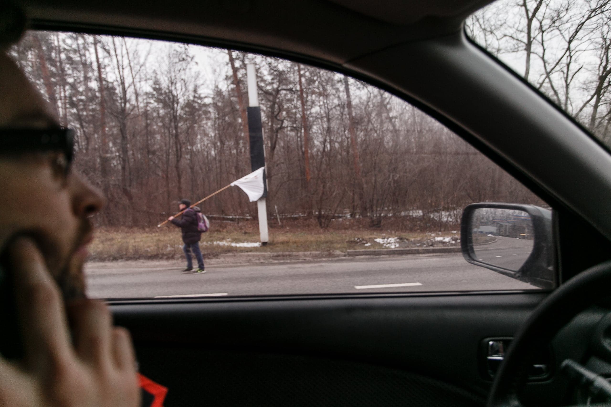 Человек с белым флагом идет по обочине дороги. Вид из автомобиля.