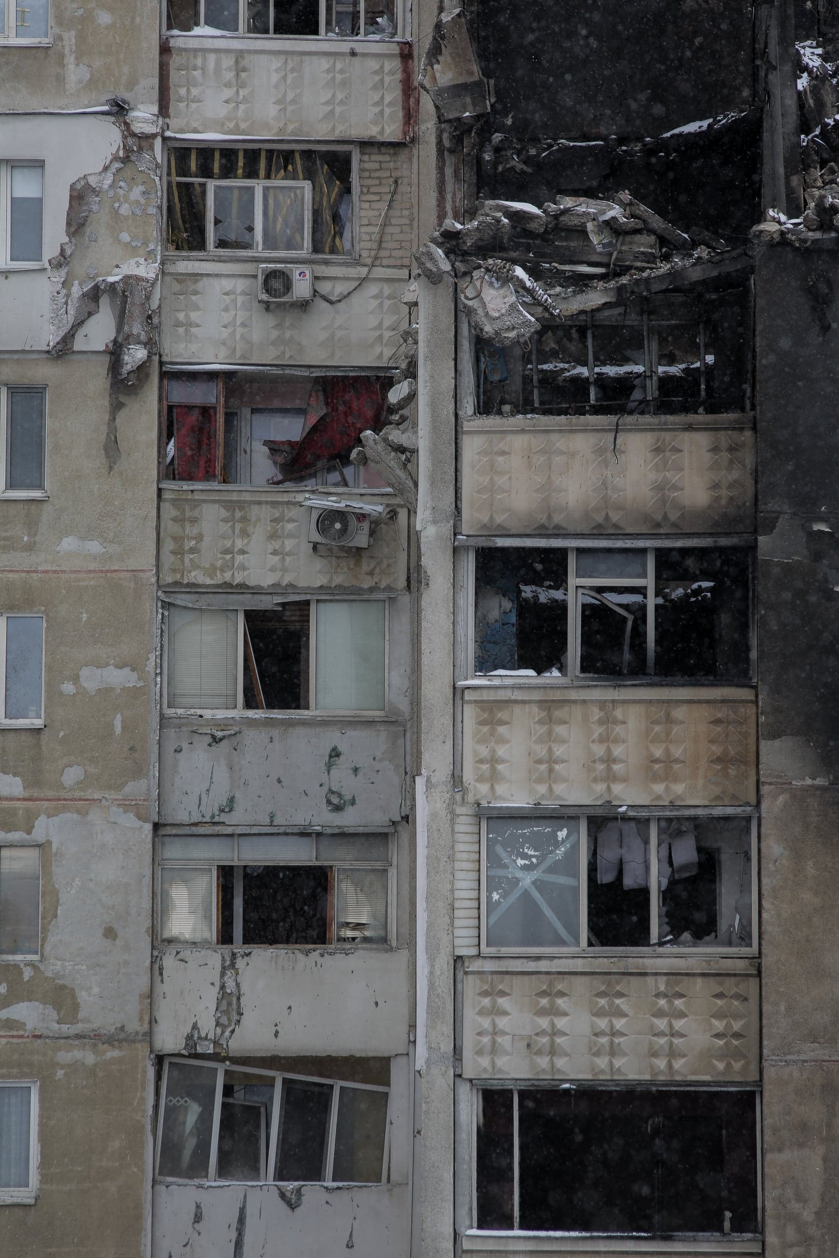 Разрушенный фасад жилого дома, выбитые окна и обрушенные балконы, следы пожара и обвалов.