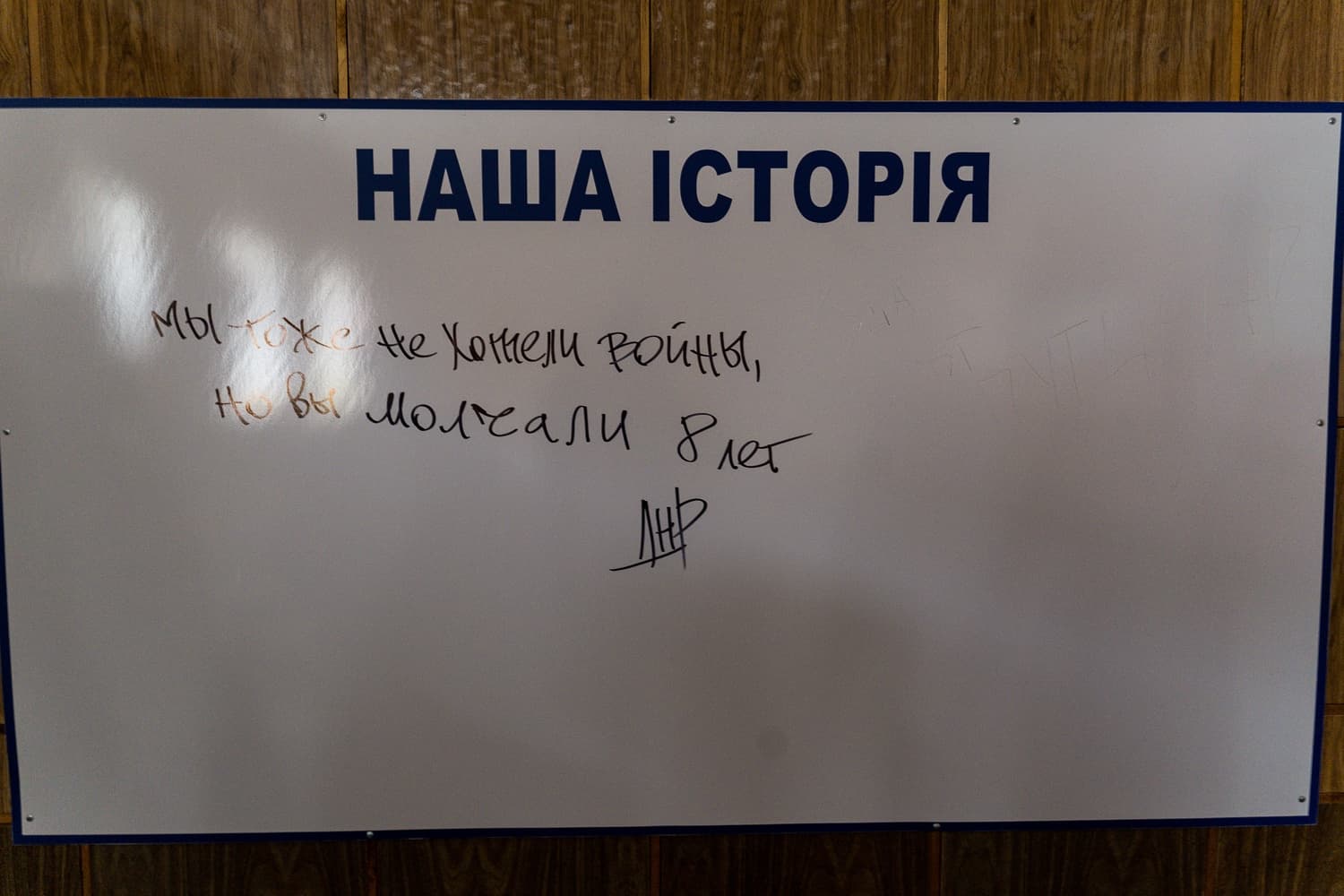 Информационный стенд с заголовком "НАША ІСТОРІЯ" и рукописной надписью: "Мы тоже не хотели войны, Но вы молчали 8 лет ЛНР".