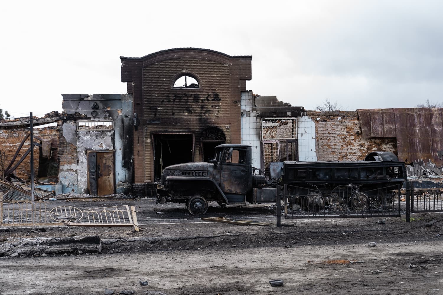 Сгоревший грузовик стоит перед разрушенным, почерневшим от огня зданием.